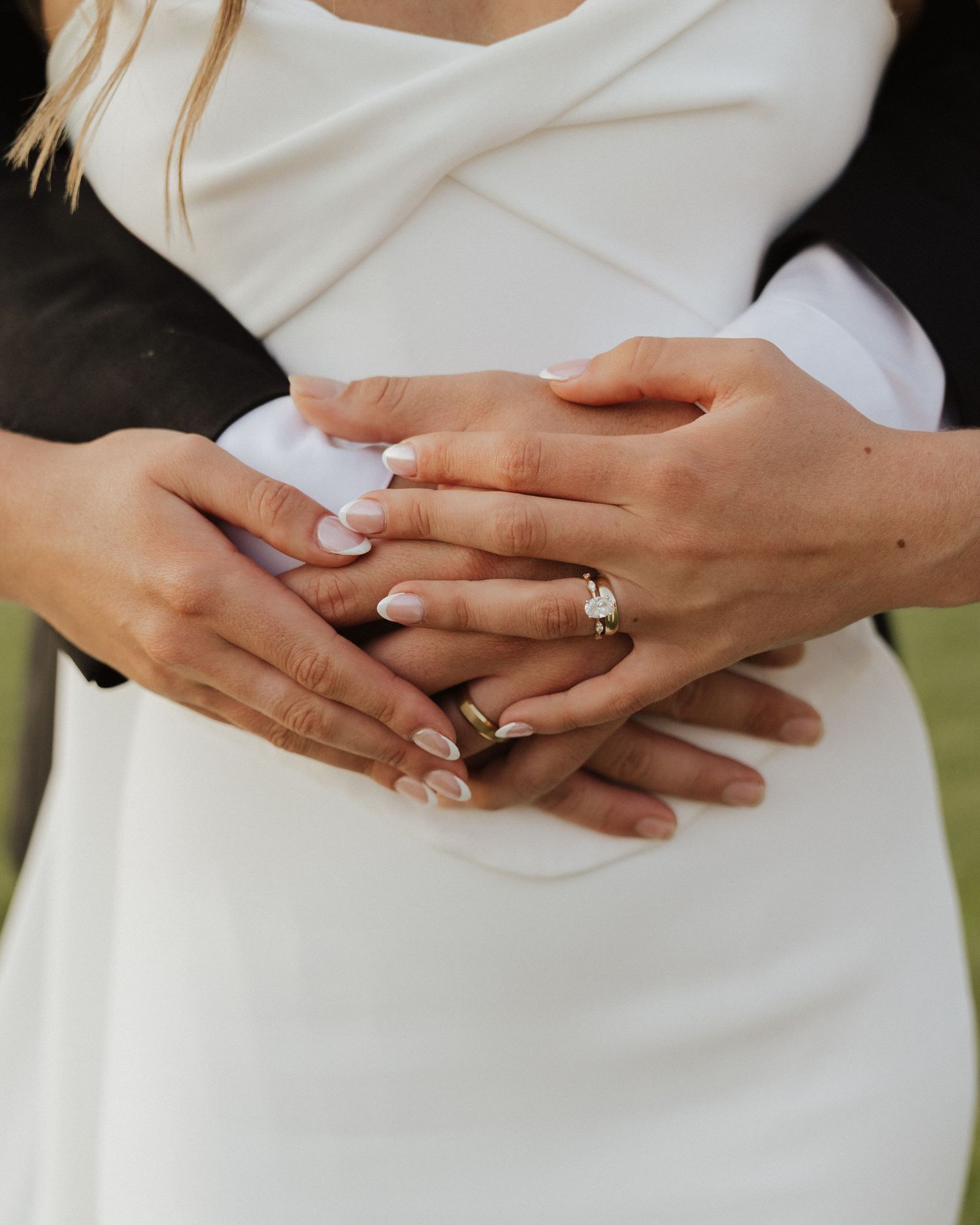 Close-up of bride and groom hands embracing showing wedding rings after outdoor ceremony.