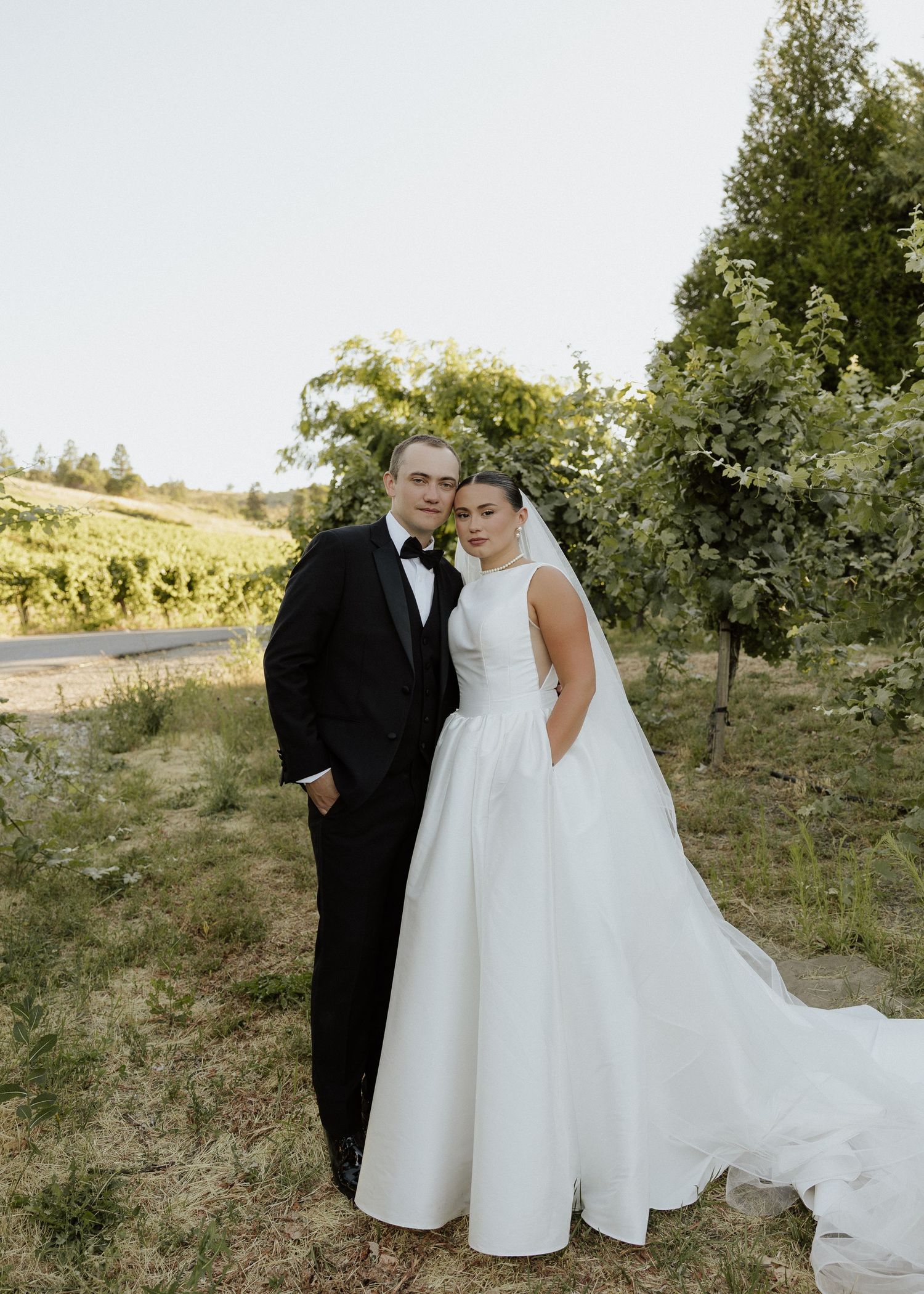 Bride and groom portrait in a vineyard, she in a ballgown with veil, he in a classic black tuxedo.