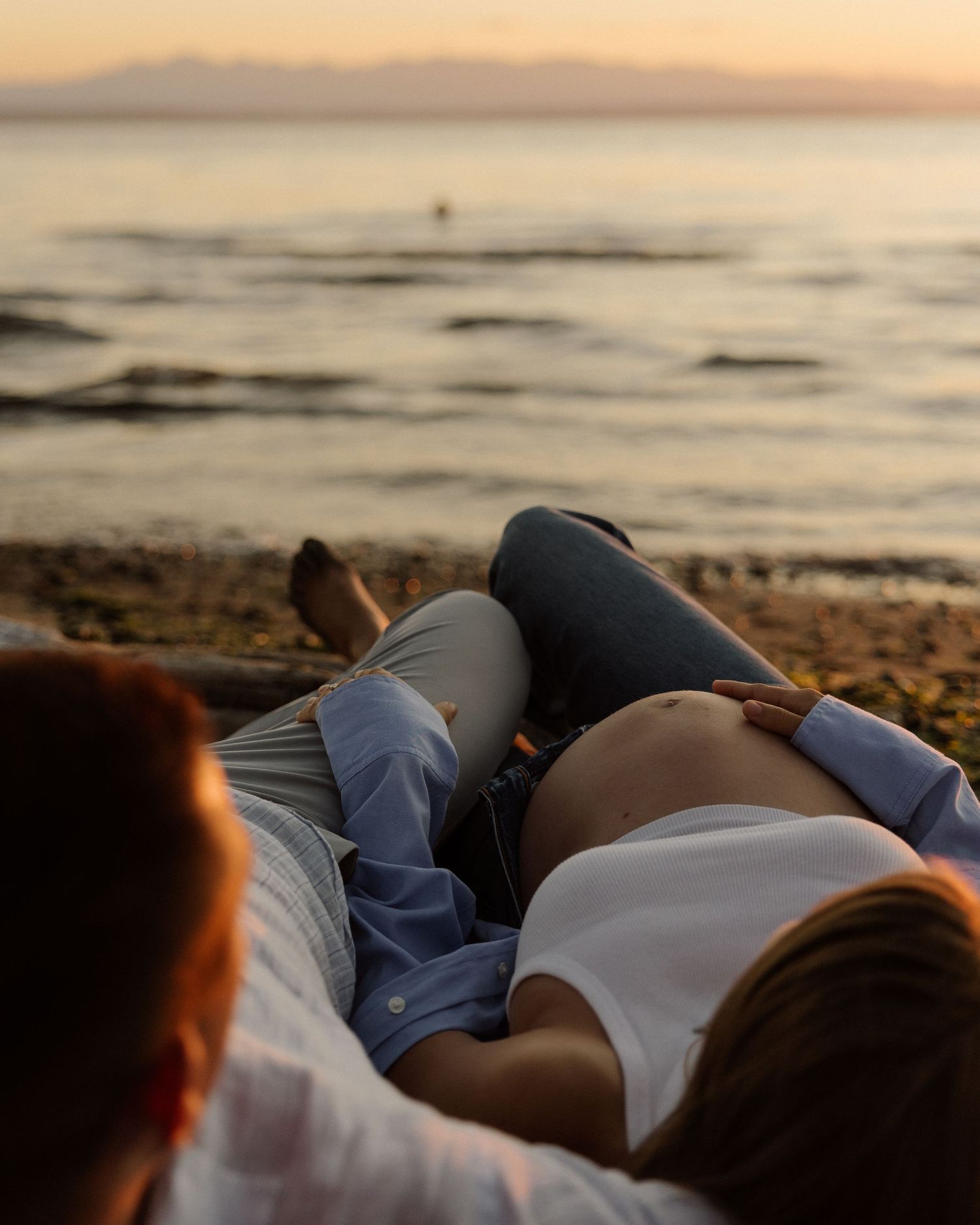 Couple lying on beach during sunset for intimate maternity photo session.