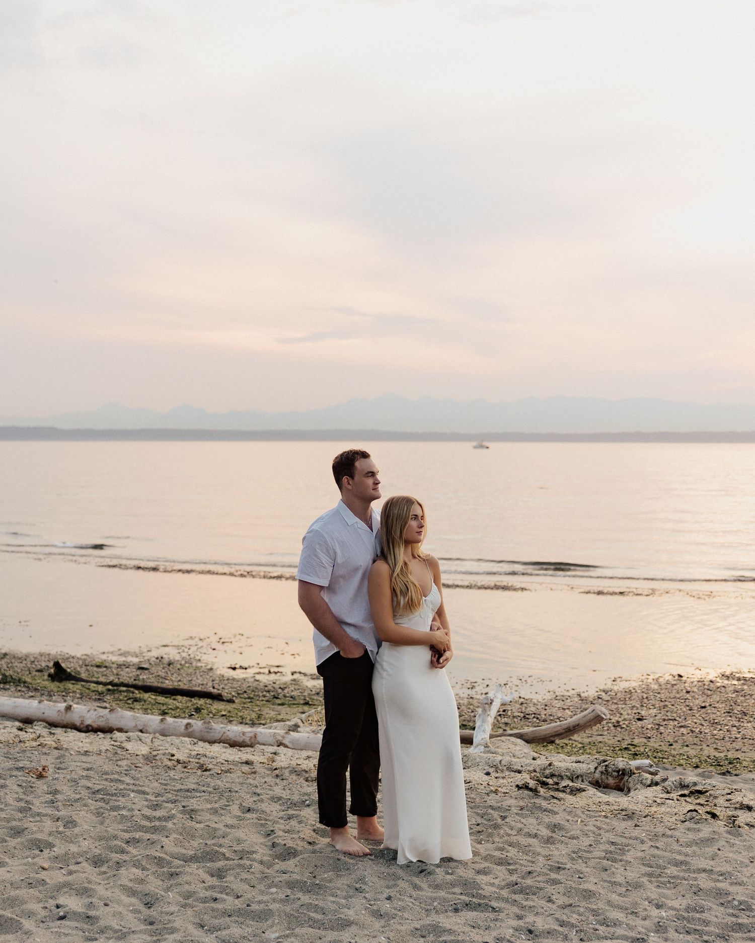 Two people embrace while standing on a beach during a peaceful sunset.