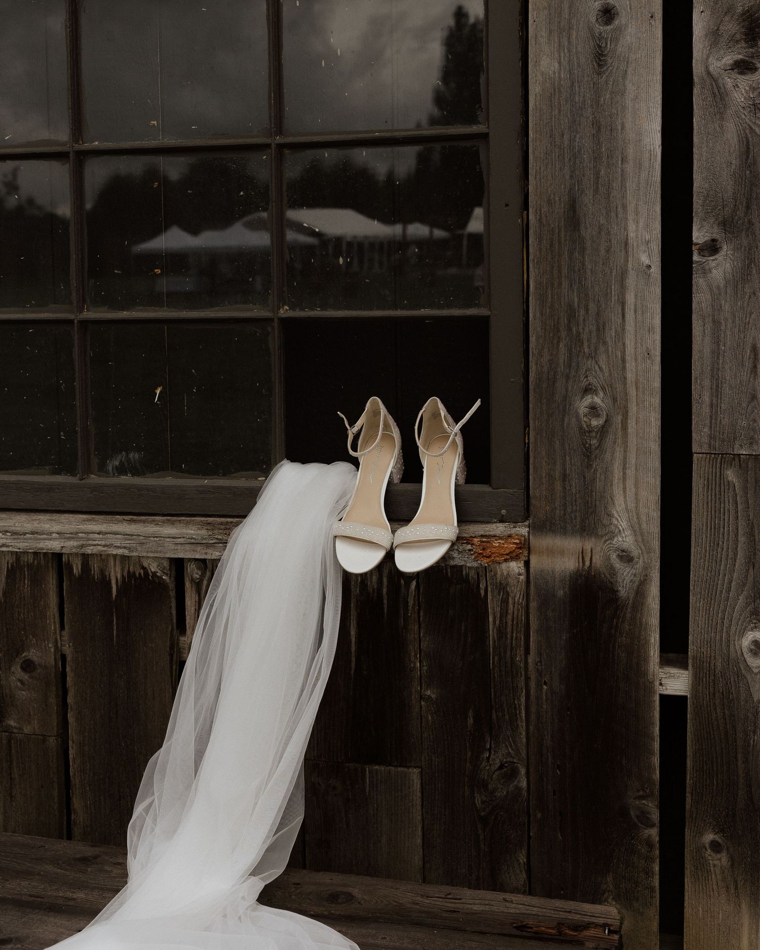 White bridal shoes and veil displayed on rustic wooden window sill.