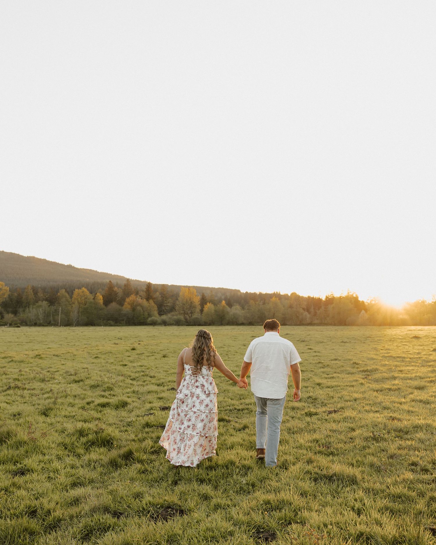 Couple walking together in sunlit meadow during golden hour.