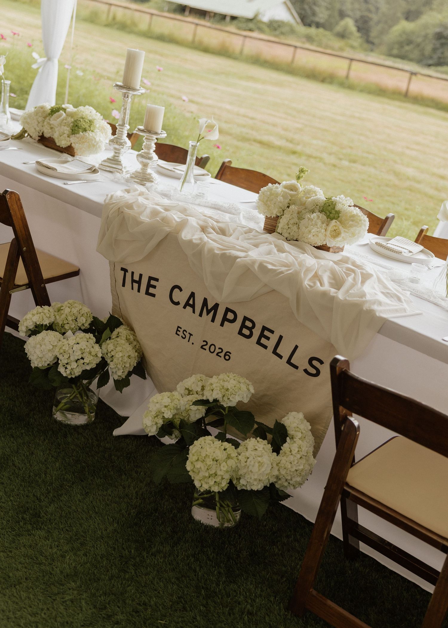 Elegant wedding sweetheart table with white hydrangeas, candles, and personalized Campbell Est. 2026 table runner.