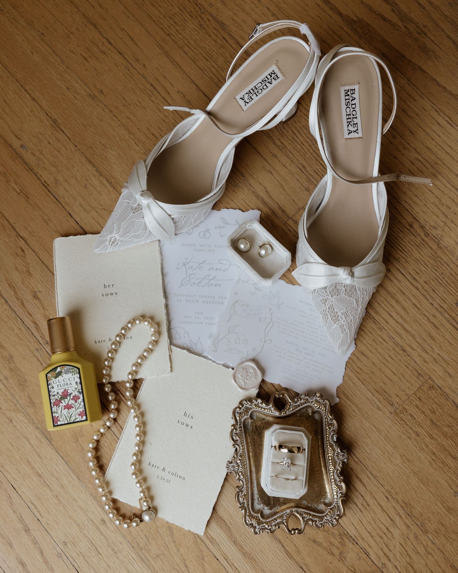 Elegant bridal flat shoes, pearl necklace, perfume, stationery, and ring display on wooden floor.
