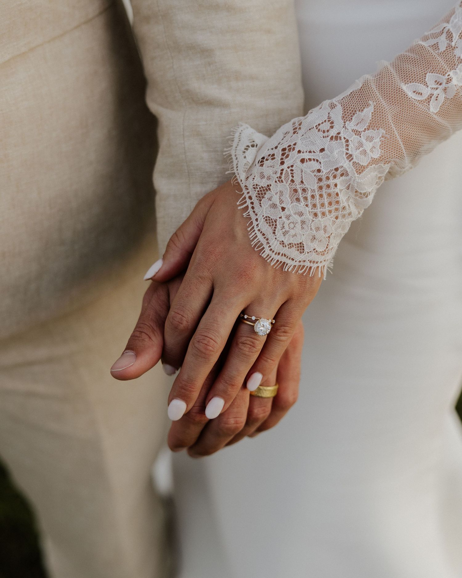 Detail shot of bride's lace sleeve and wedding rings as couple holds hands.