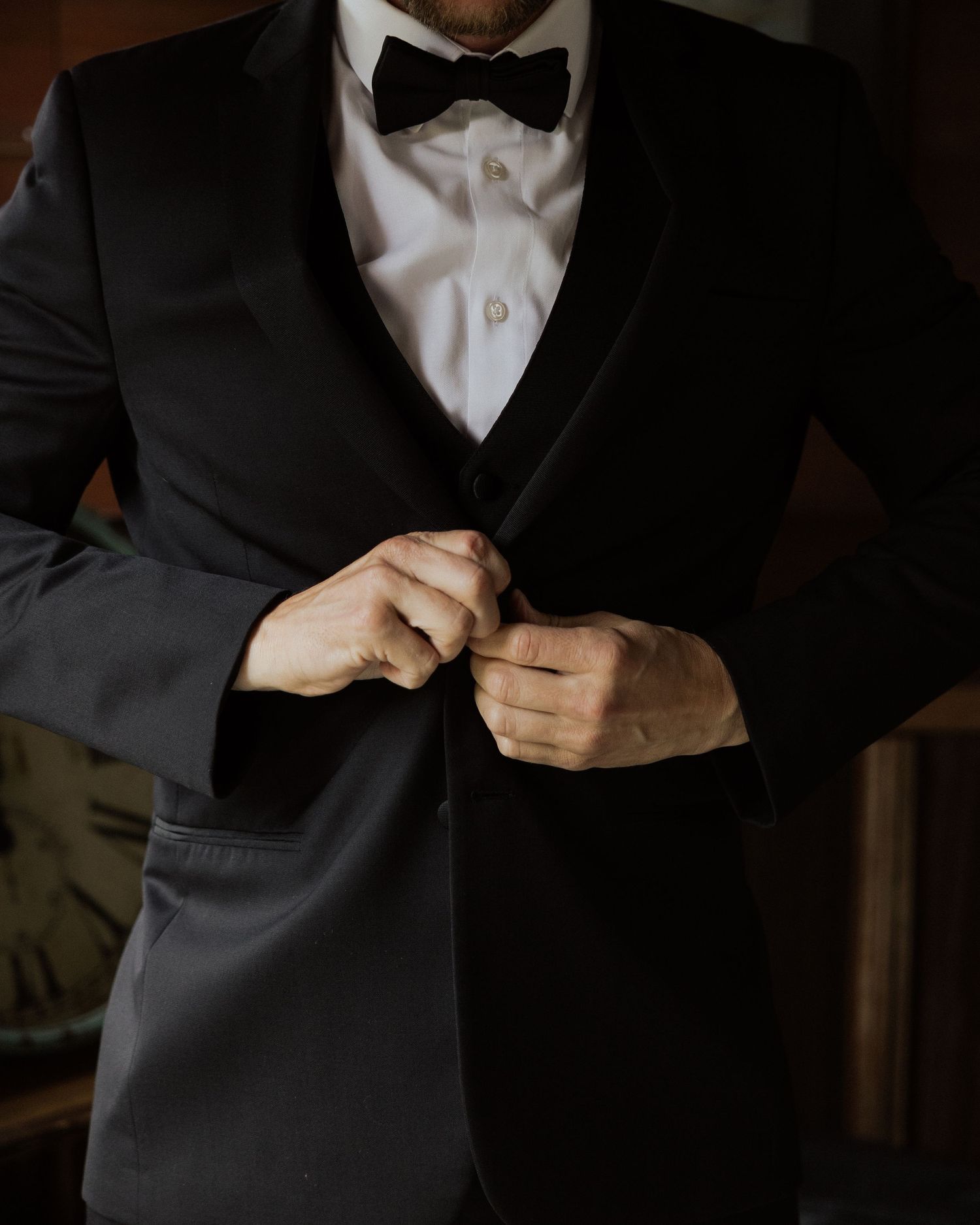 Close-up of hands adjusting black bow tie and formal tuxedo jacket.