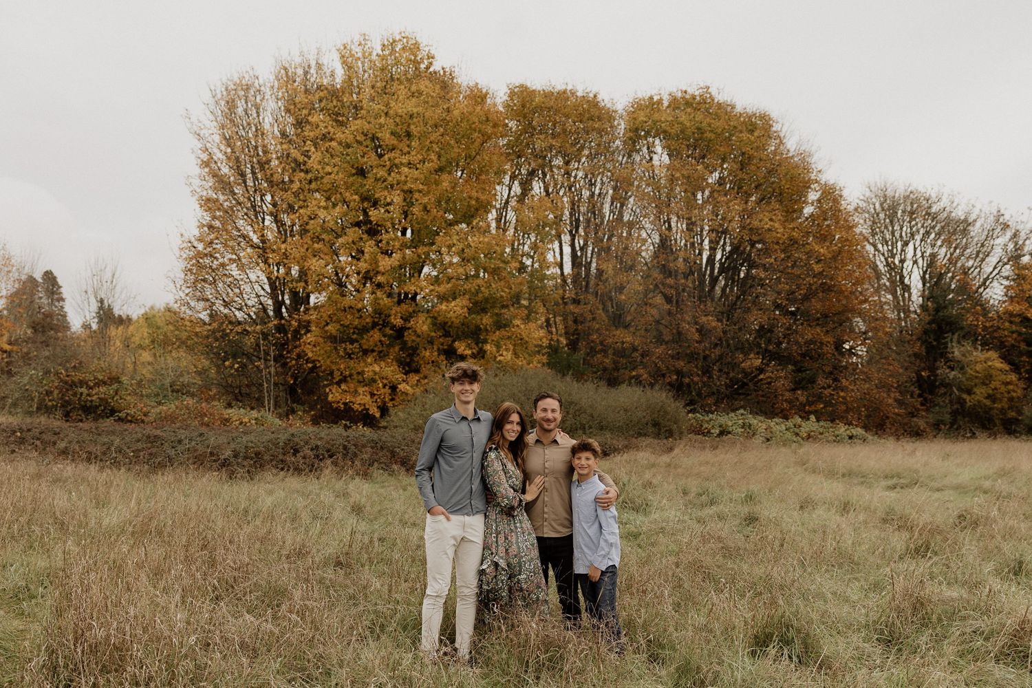 Candid outdoor photo session in a field with golden autumn trees behind.