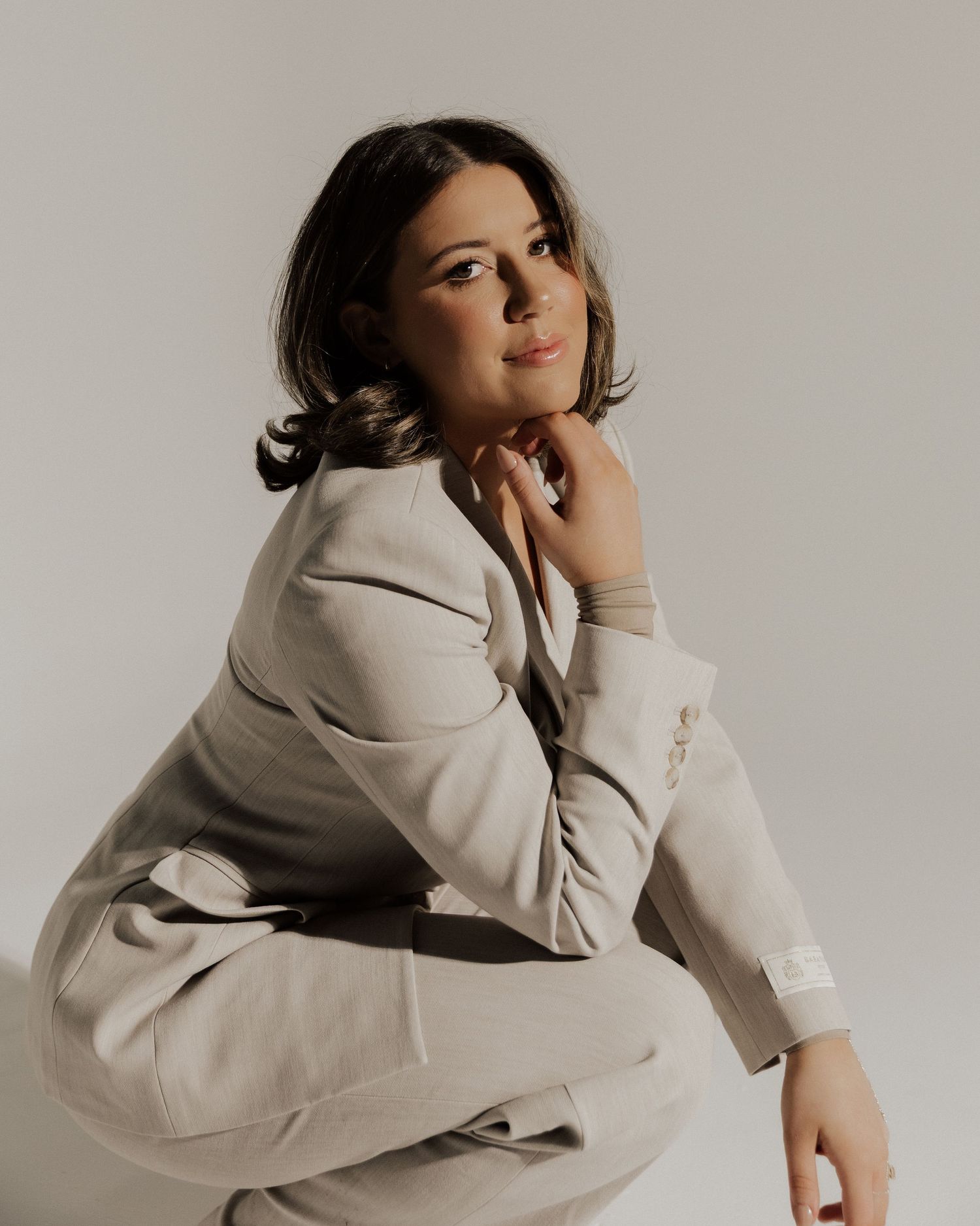 Stylish portrait of someone in a beige suit posing against a light background.