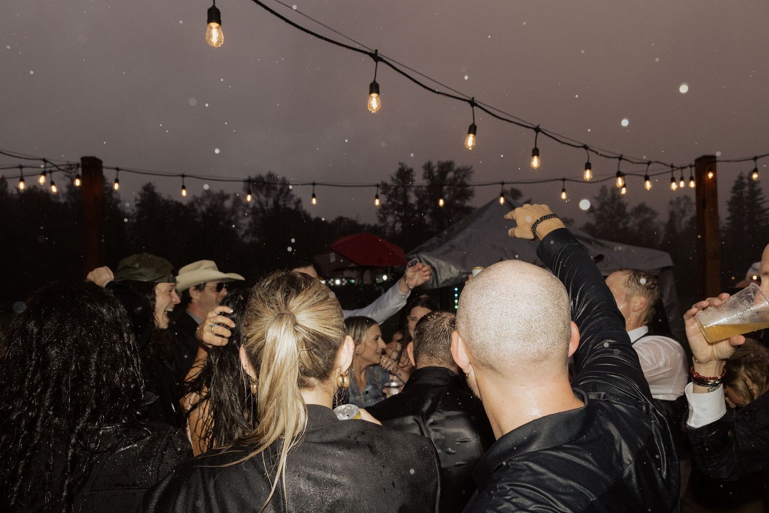 Outdoor evening party with string lights and a crowd of people dancing under the night sky.