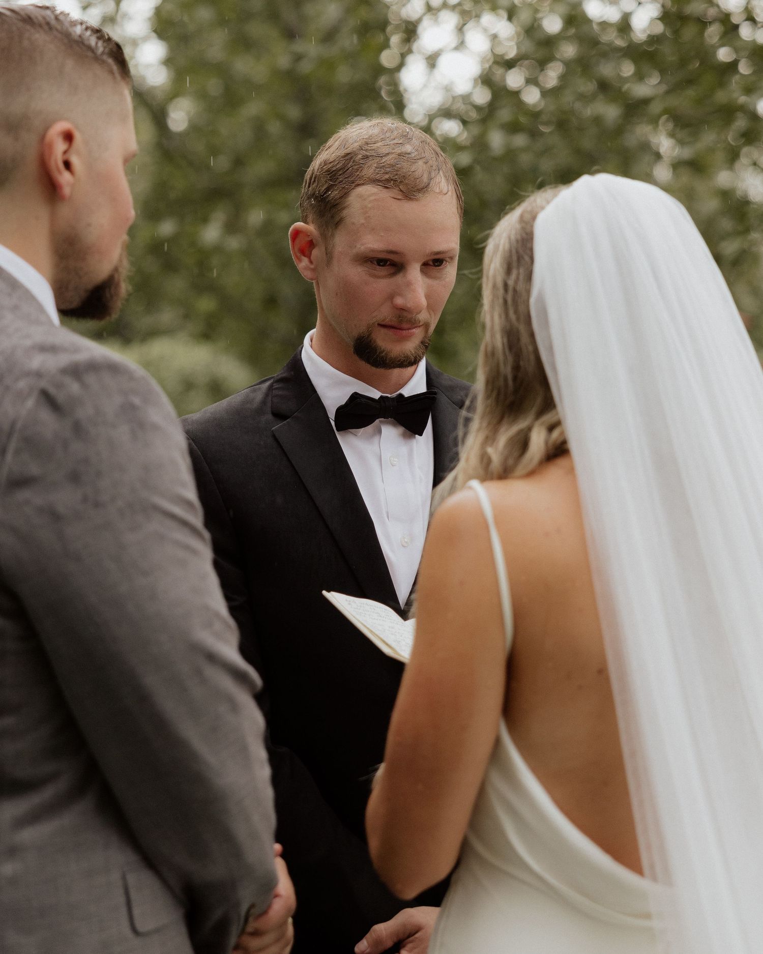 Wedding ceremony moment showing exchange of vows under outdoor pergola.