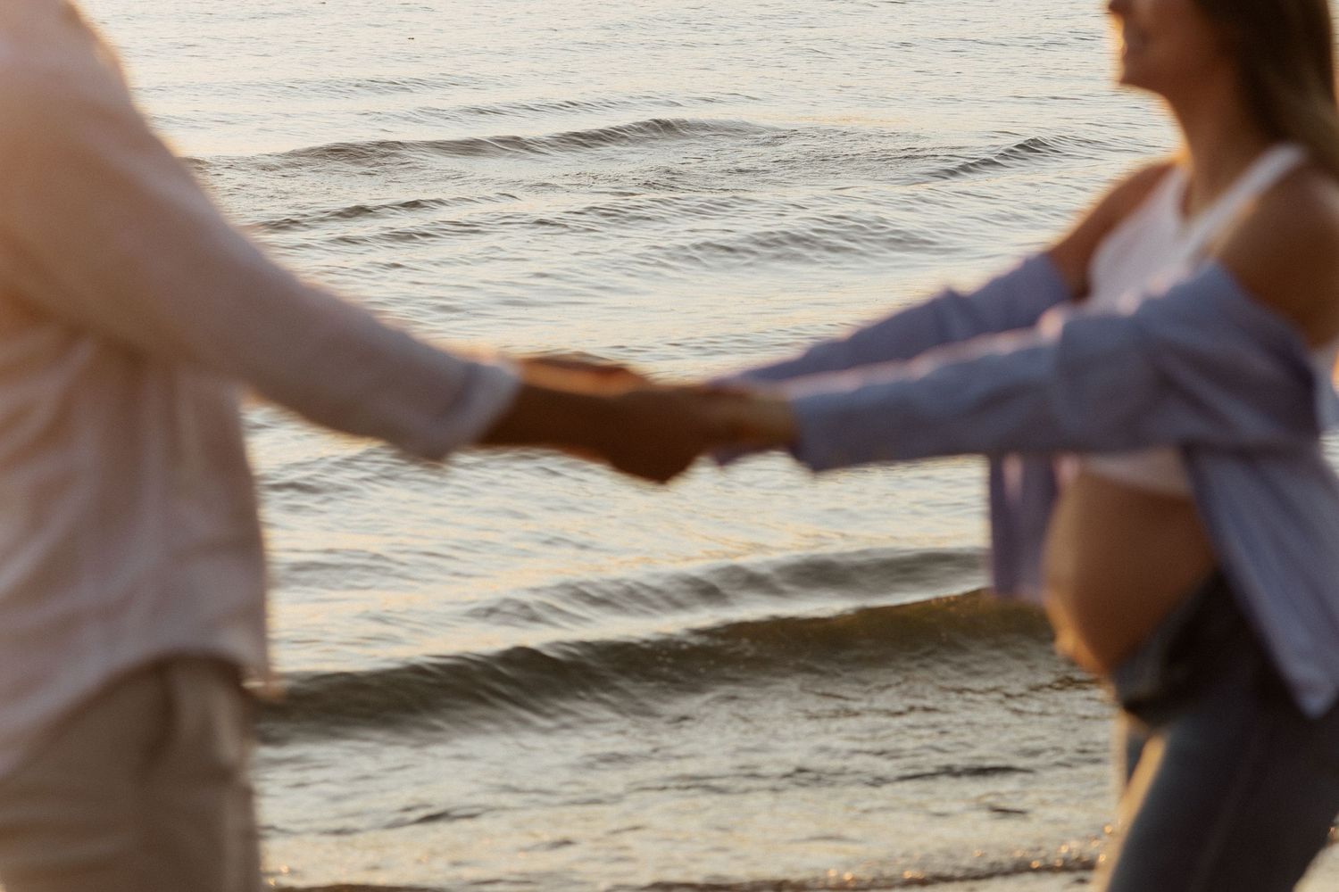 Silhouetted couple holding hands against sunset ocean waves.