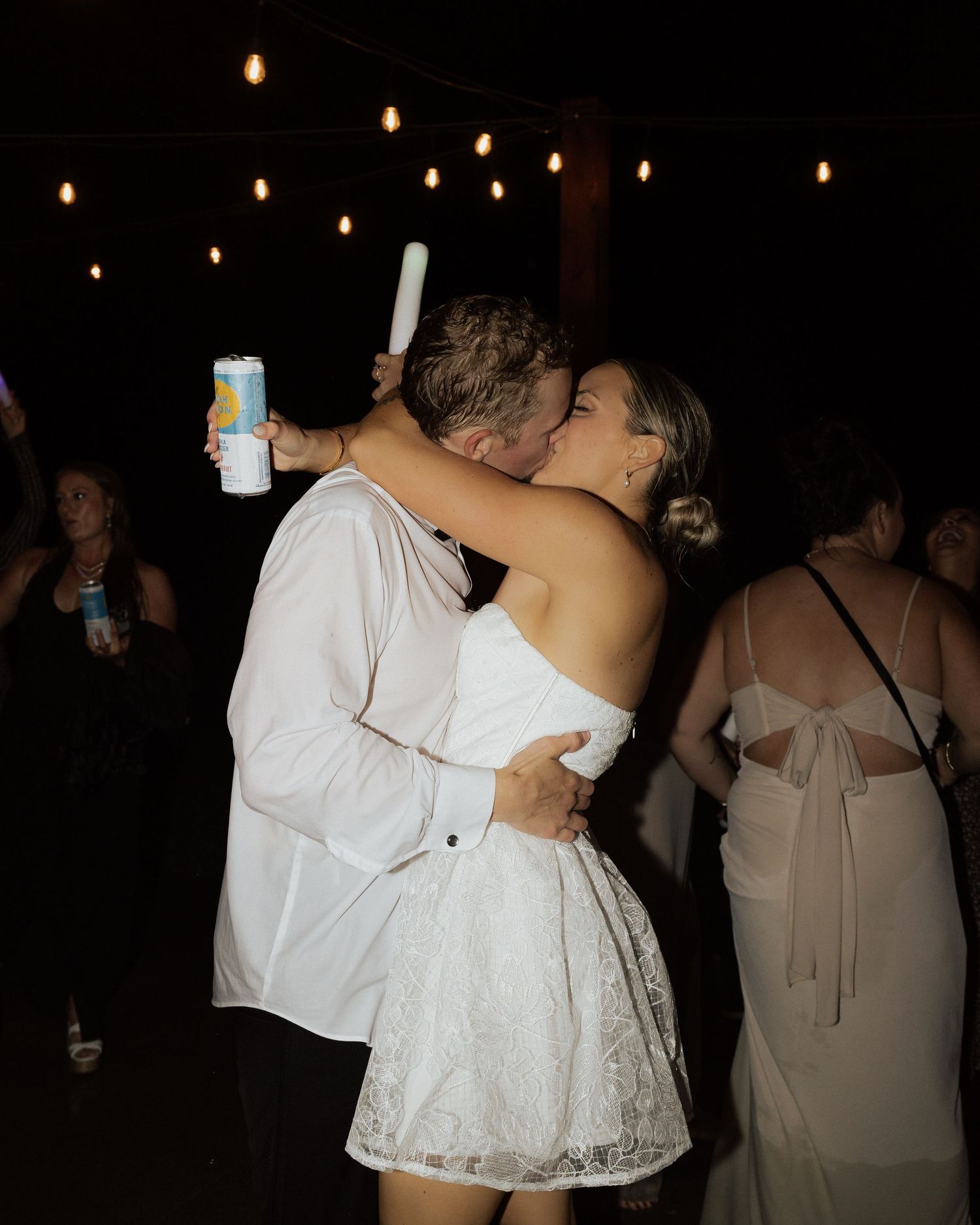 A couple embracing on the dance floor at an outdoor wedding reception under string lights.