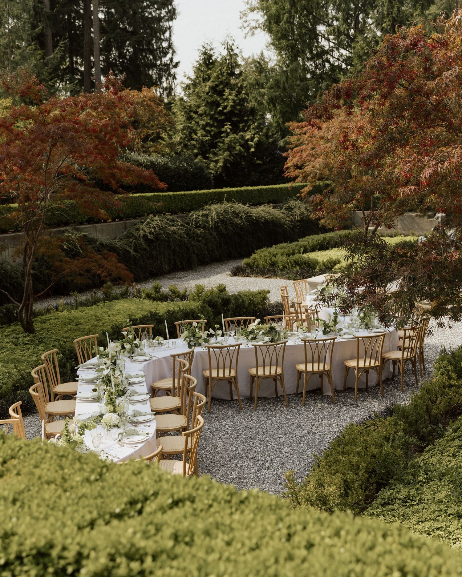 Elegant outdoor wedding reception with gold chairs and greenery centerpieces set in a manicured garden with autumn foliage.