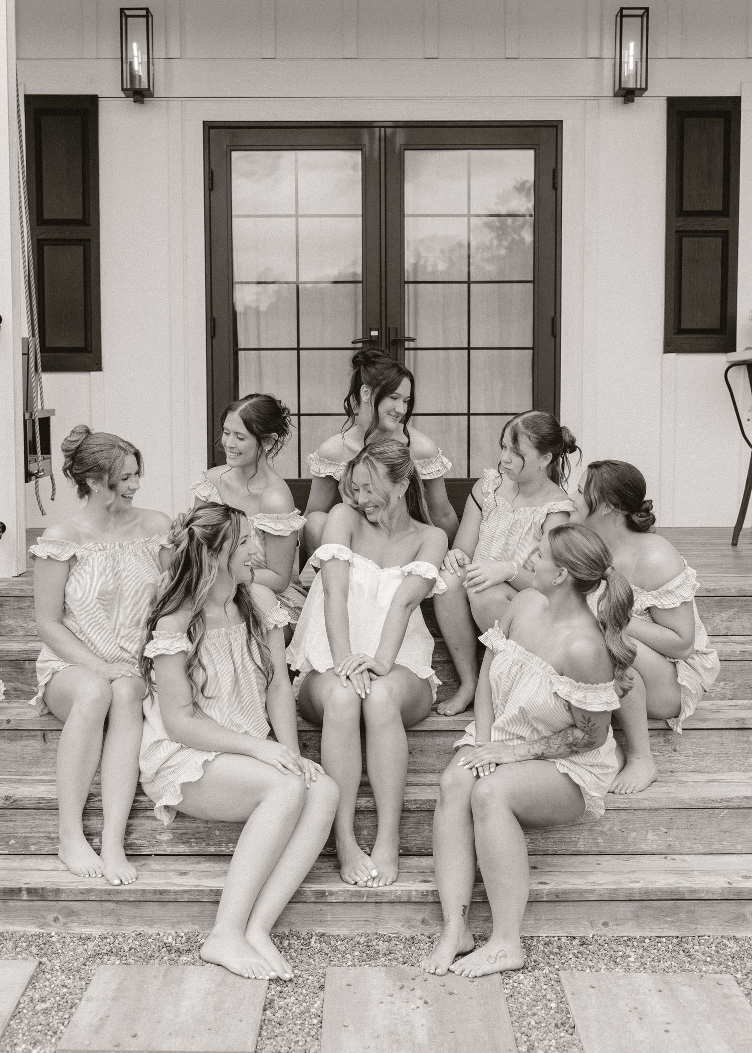 Black and white photo of a bride in a corset surrounded by bridesmaids in matching dresses on outdoor steps.