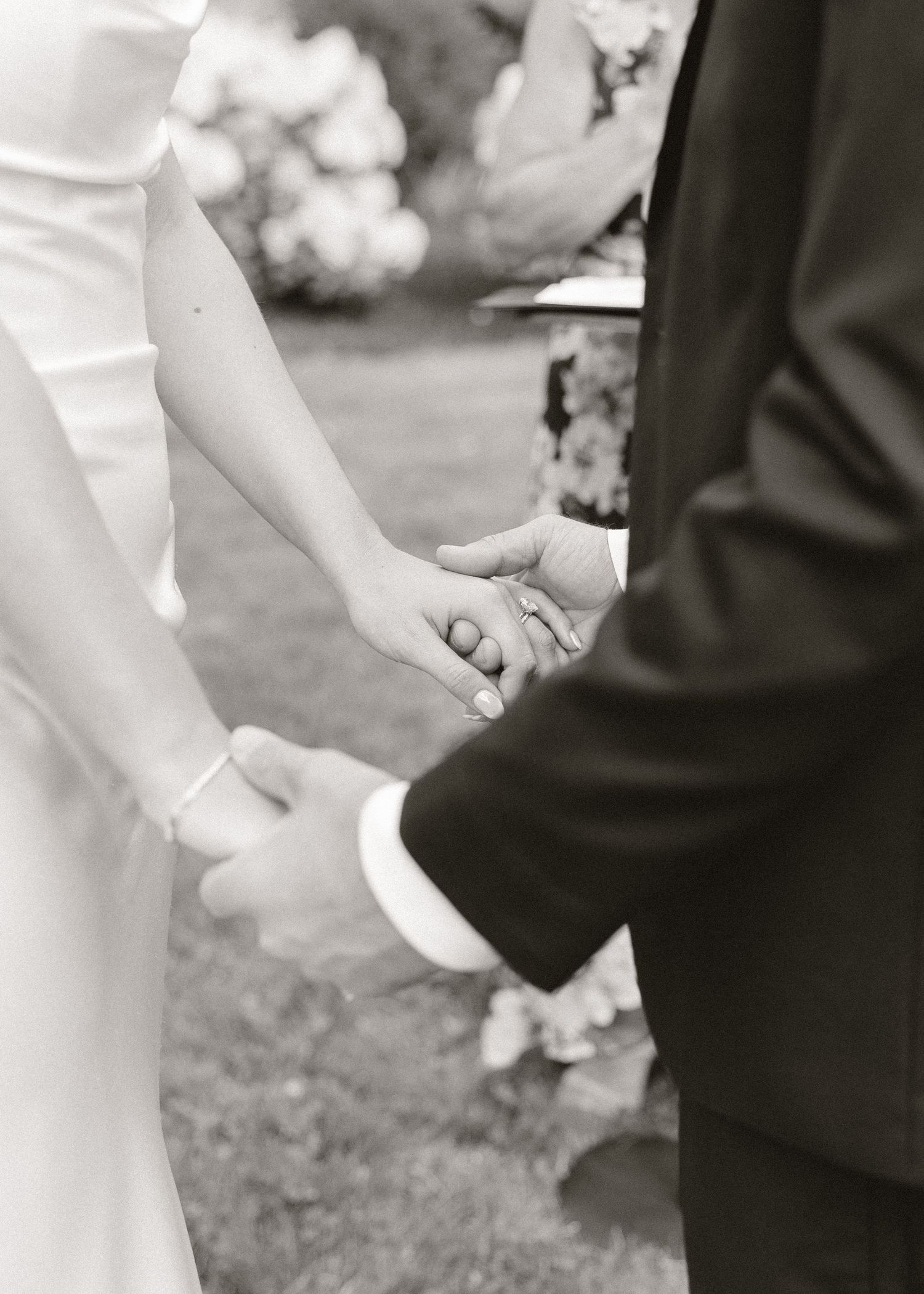 Black and white photo of bride and groom holding hands during outdoor wedding ceremony.