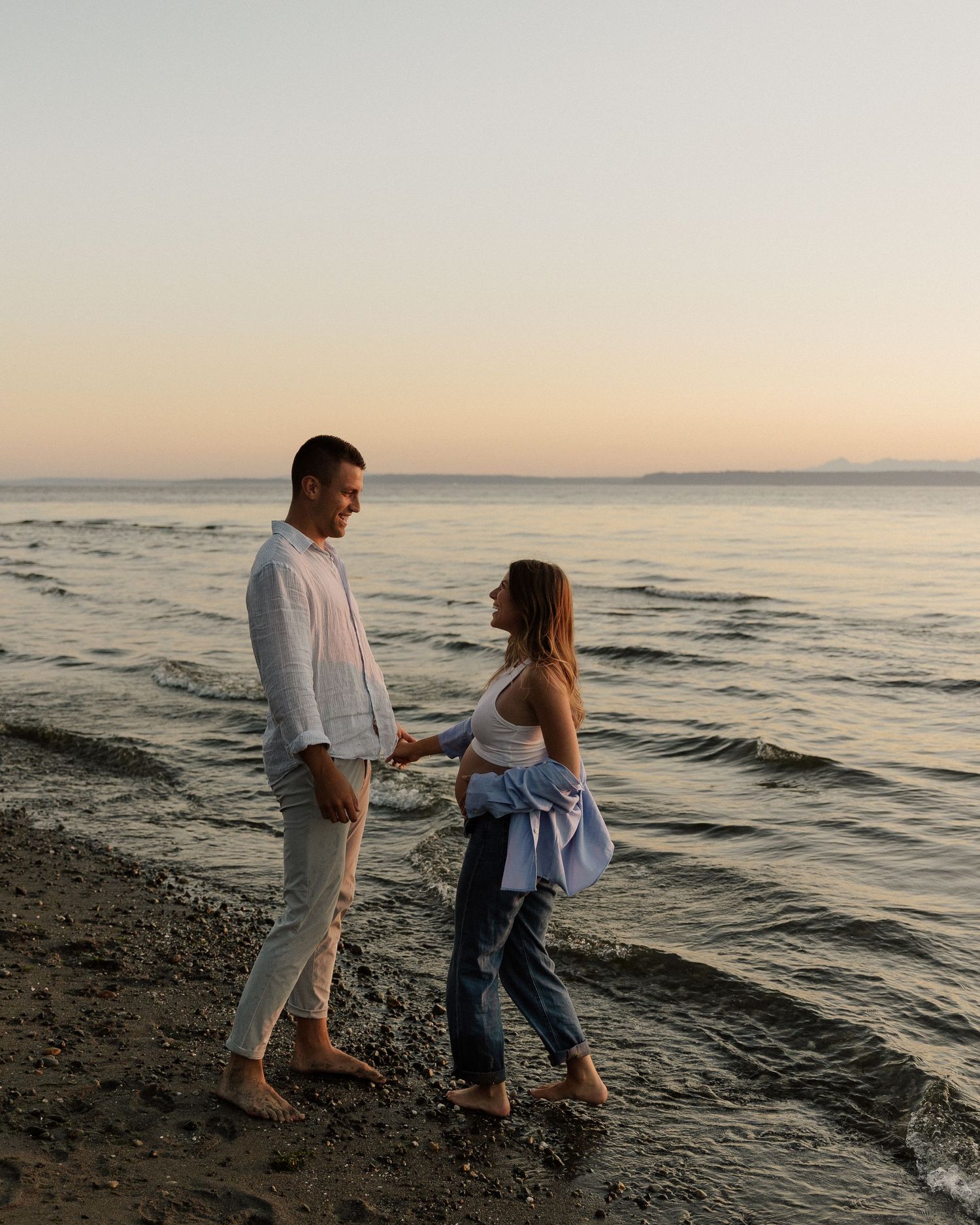 Two people enjoying an intimate moment while walking barefoot on the beach at dusk.