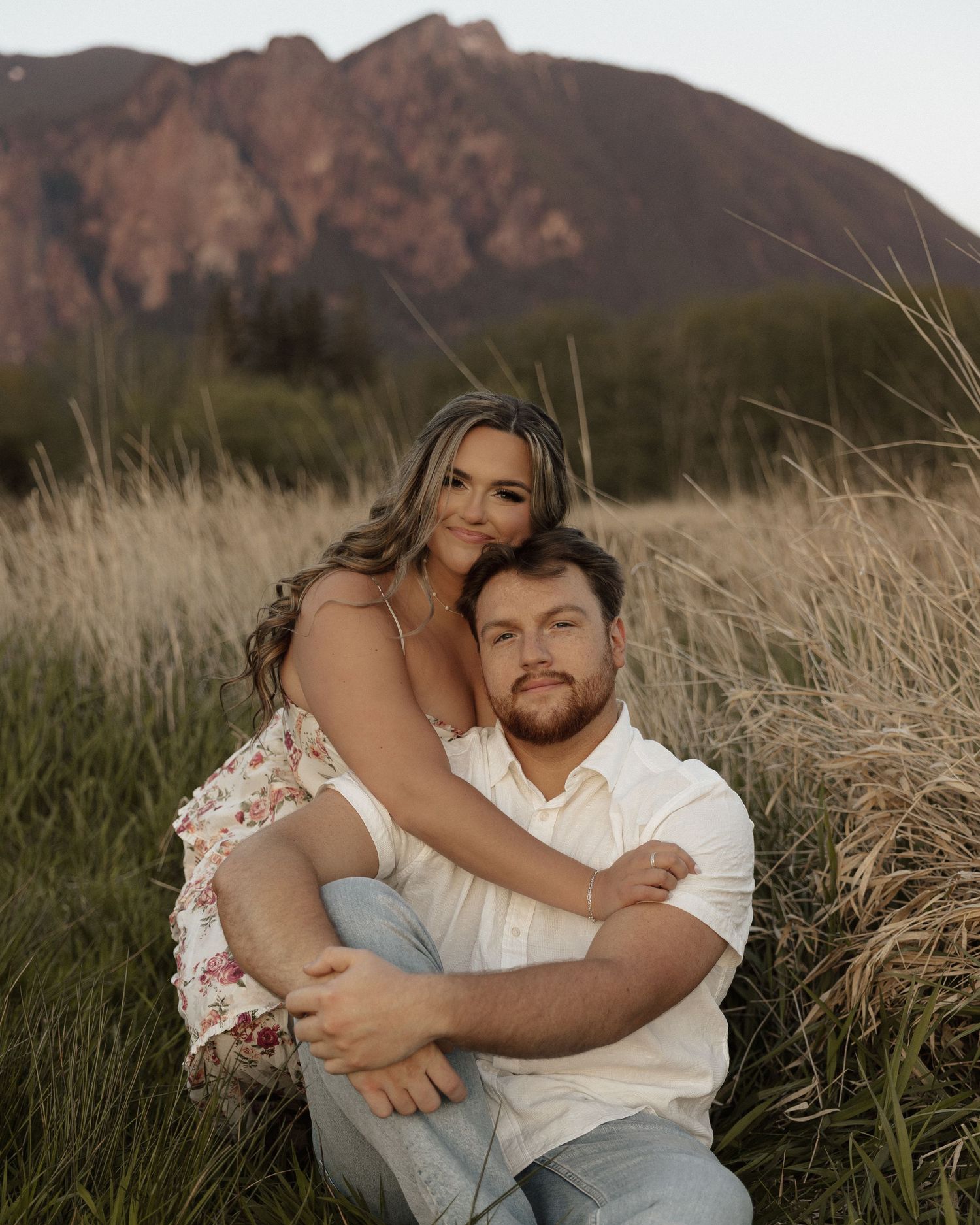 Intimate portrait of couple in golden field with mountain backdrop.