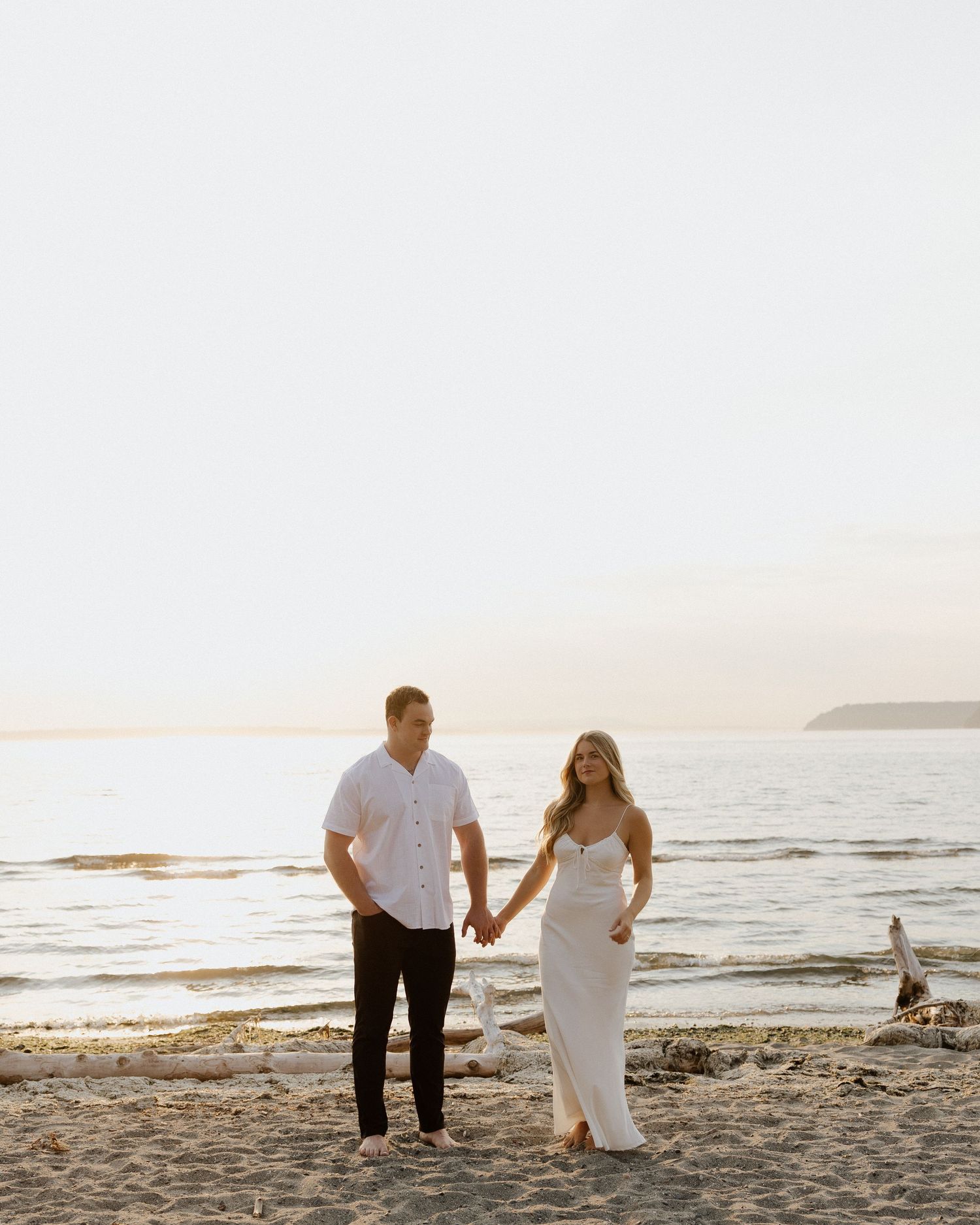 A couple walks hand in hand along a scenic beach during sunset.