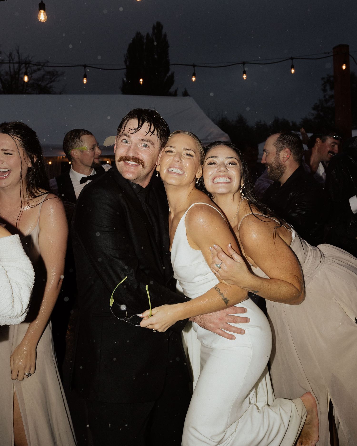 Energetic dancing and celebration at an outdoor wedding reception under string lights.