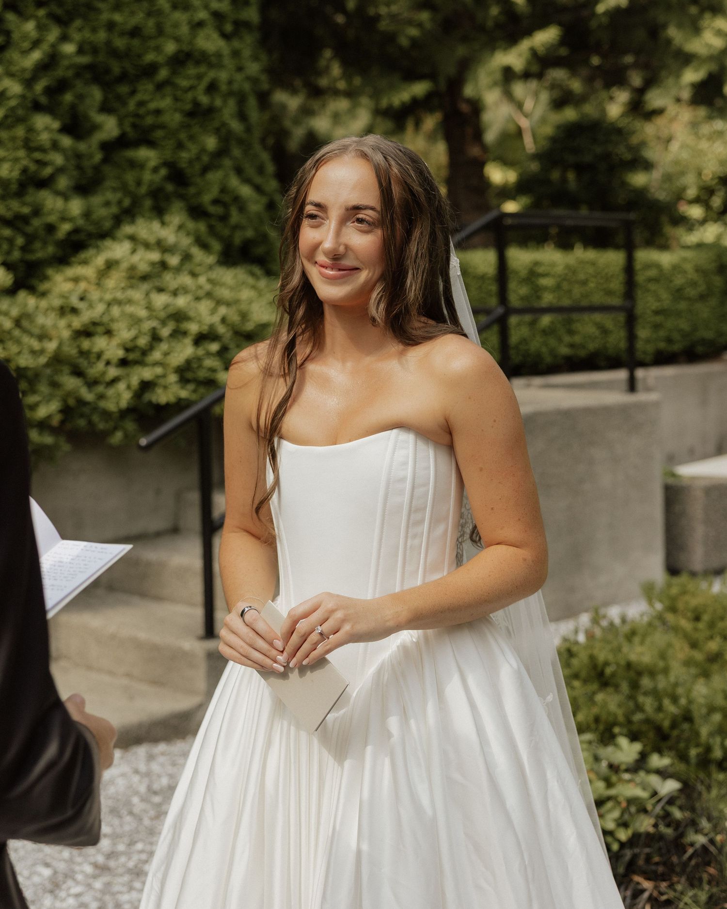 Bride in strapless white corset wedding gown smiling during outdoor ceremony.