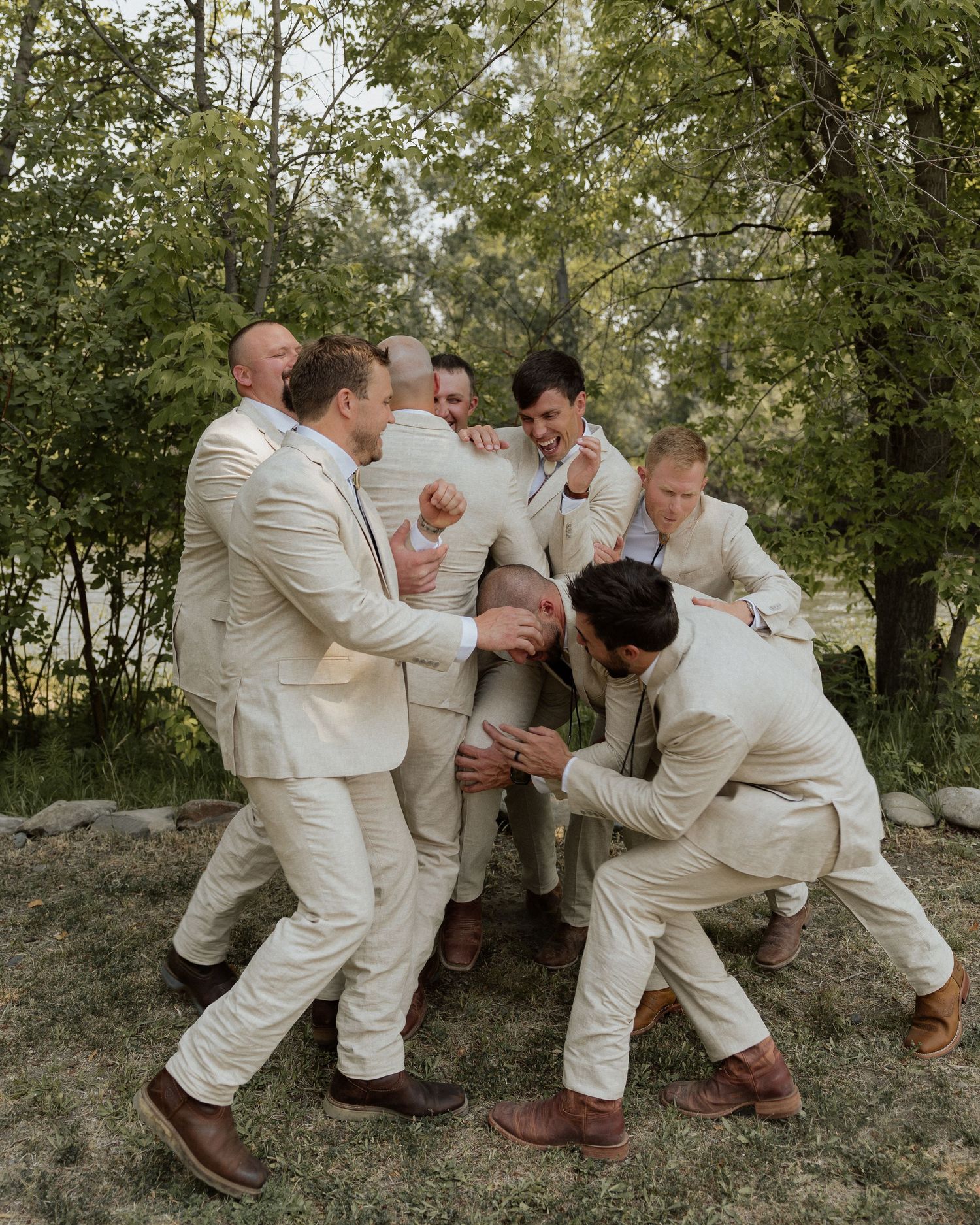 Group in cream colored suits playfully posing outdoors in a woodsy setting.