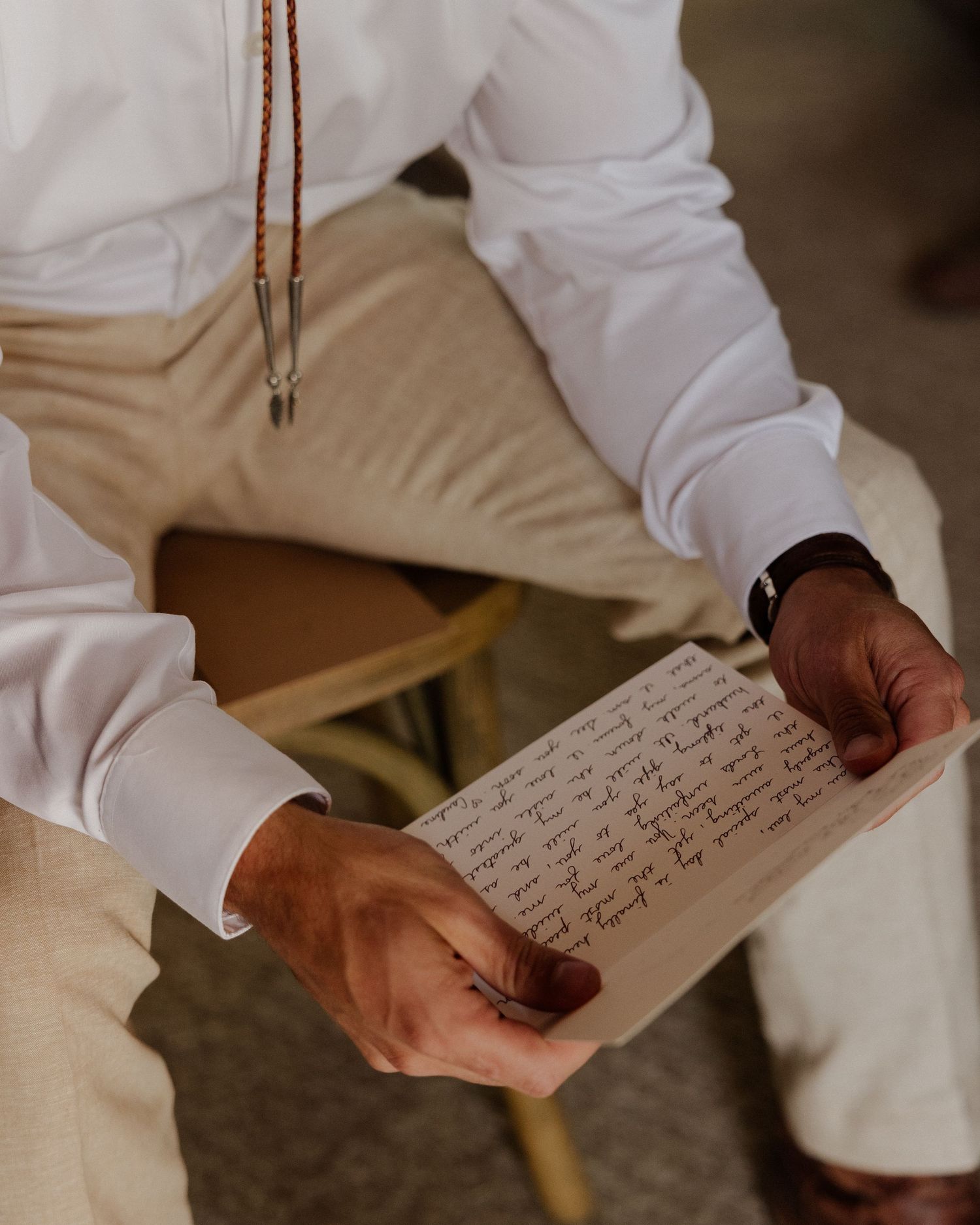 Hands holding handwritten note while wearing white formal attire and khaki pants.