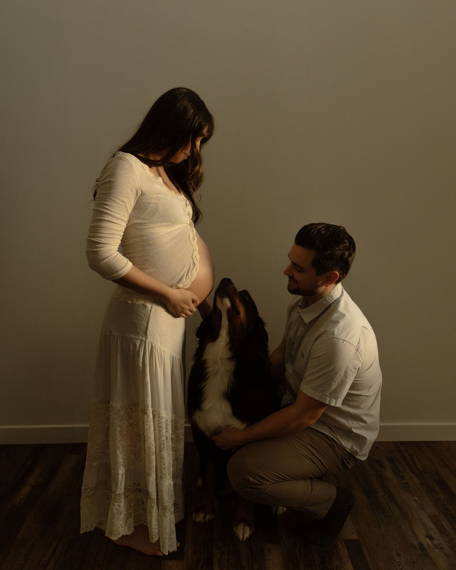 Maternity photo featuring couple and their dog in minimalist indoor setting.