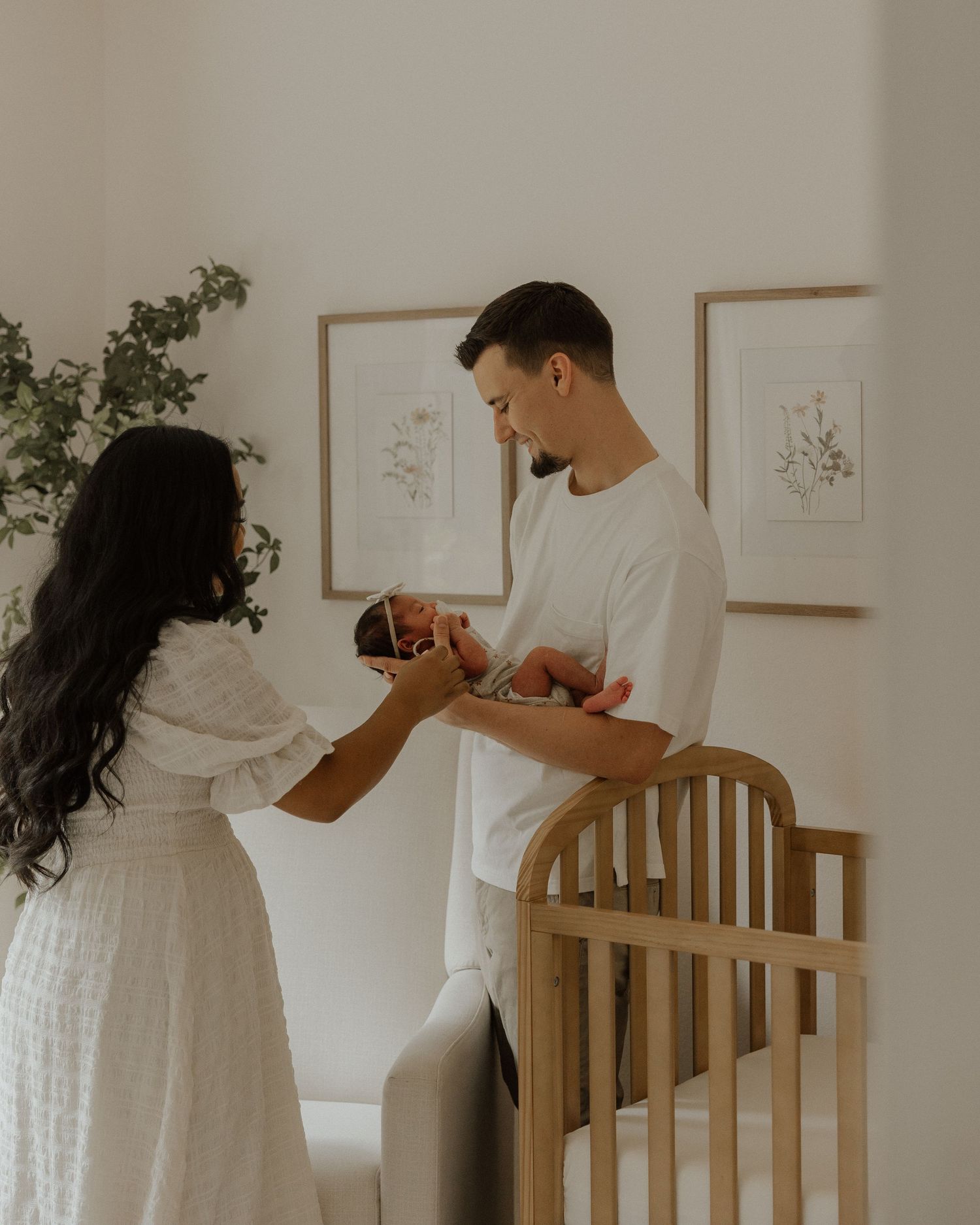 Parents standing by wooden crib sharing moment with newborn in bright nursery.