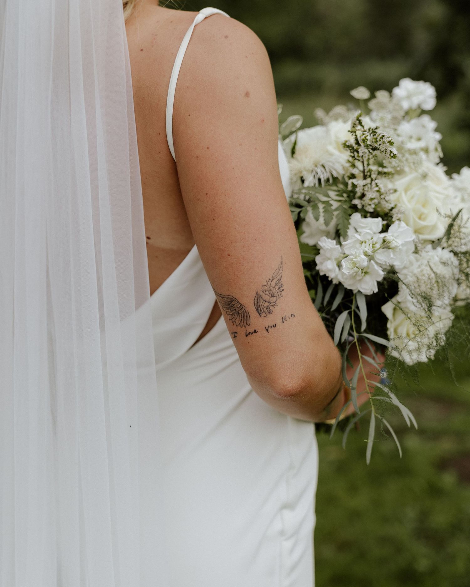 Detail shot of bride's butterfly tattoo and white bouquet against wedding dress.