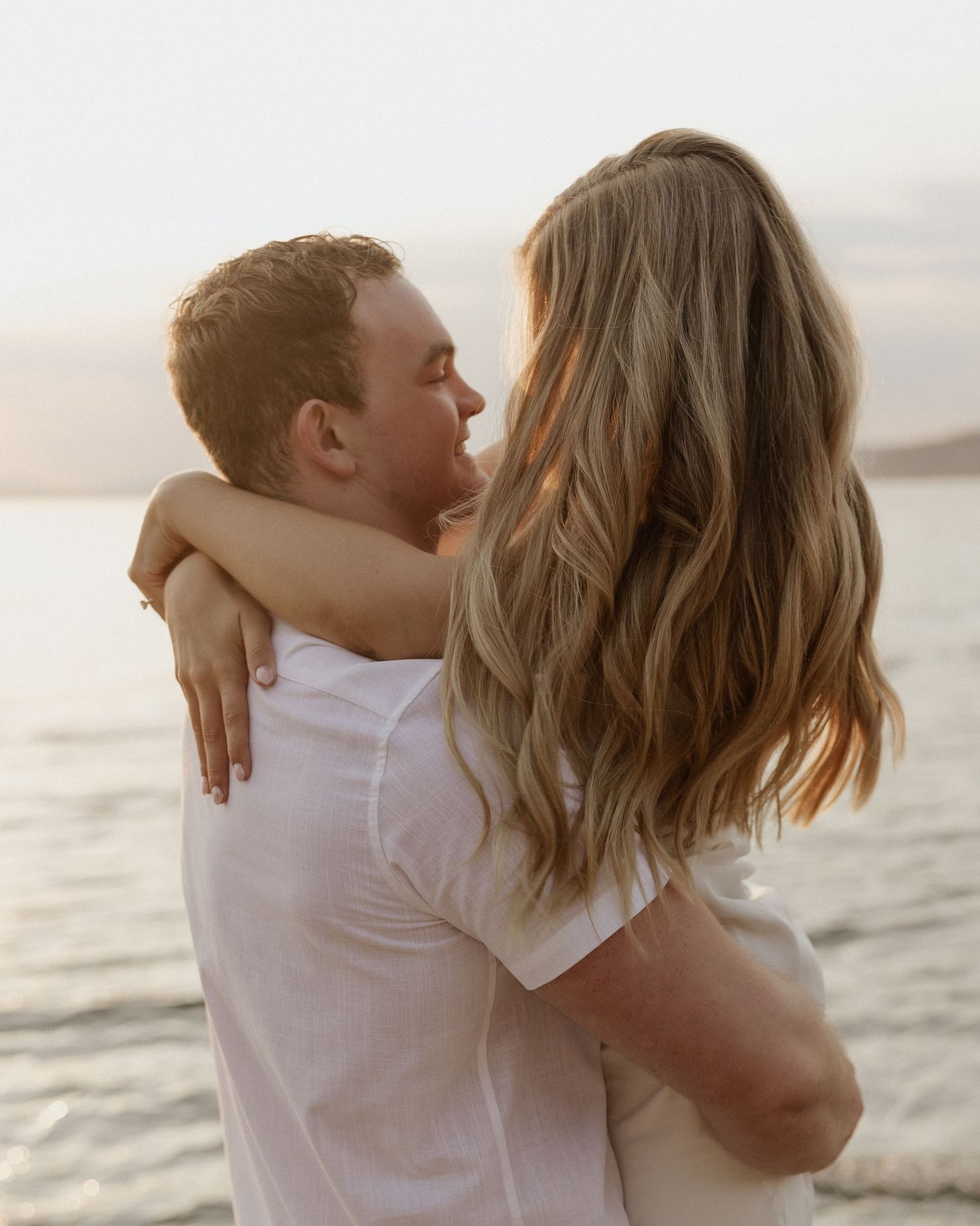 Couple in white sharing intimate embrace on beach during golden hour.