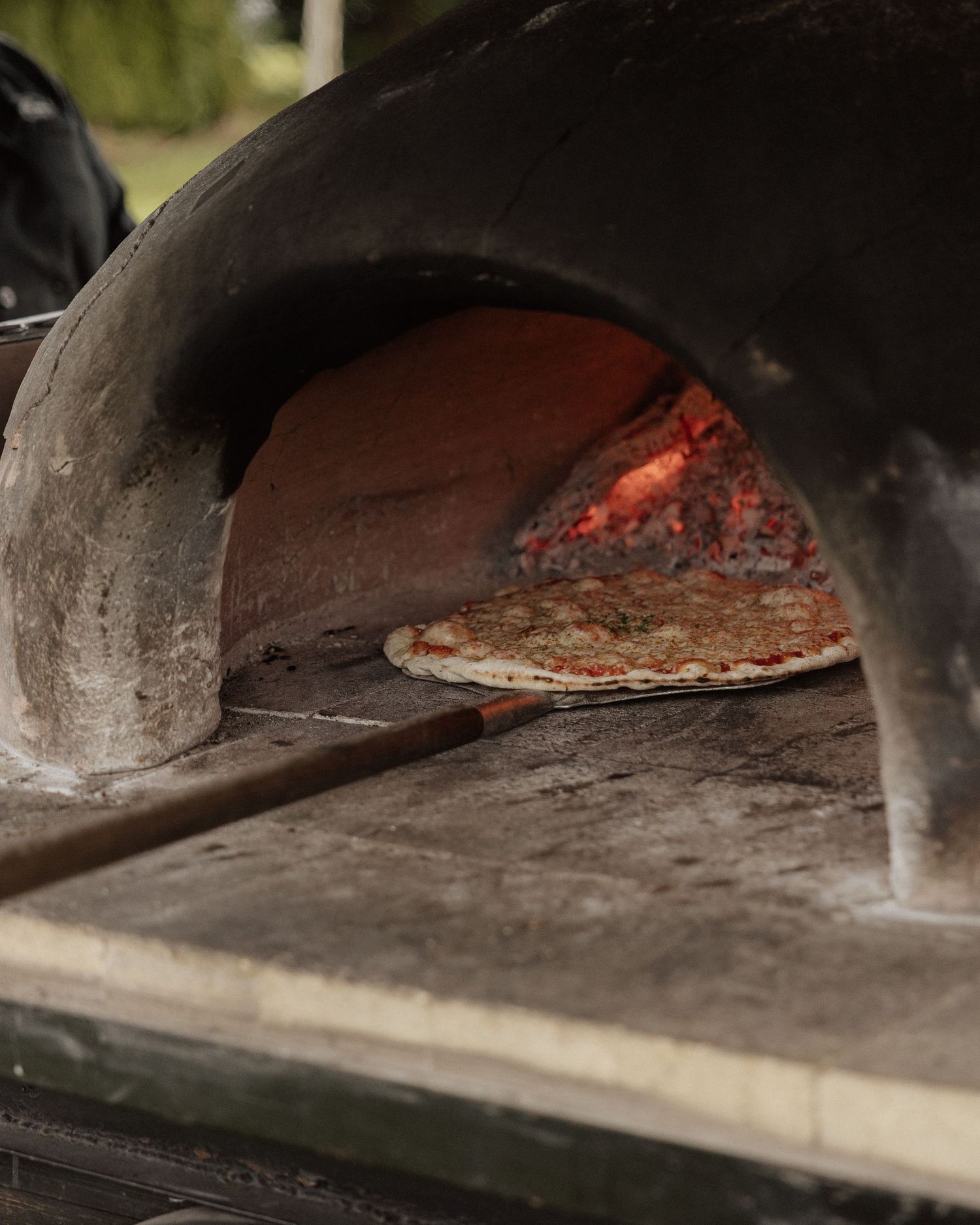Wood-fired pizza baking in a traditional brick oven with glowing embers visible.