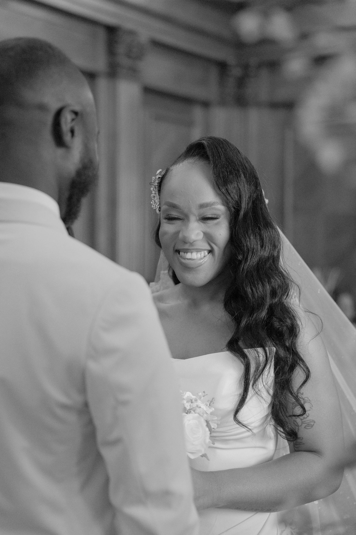 A bride in a white wedding dress smiles joyfully during an intimate black and white wedding ceremony moment.