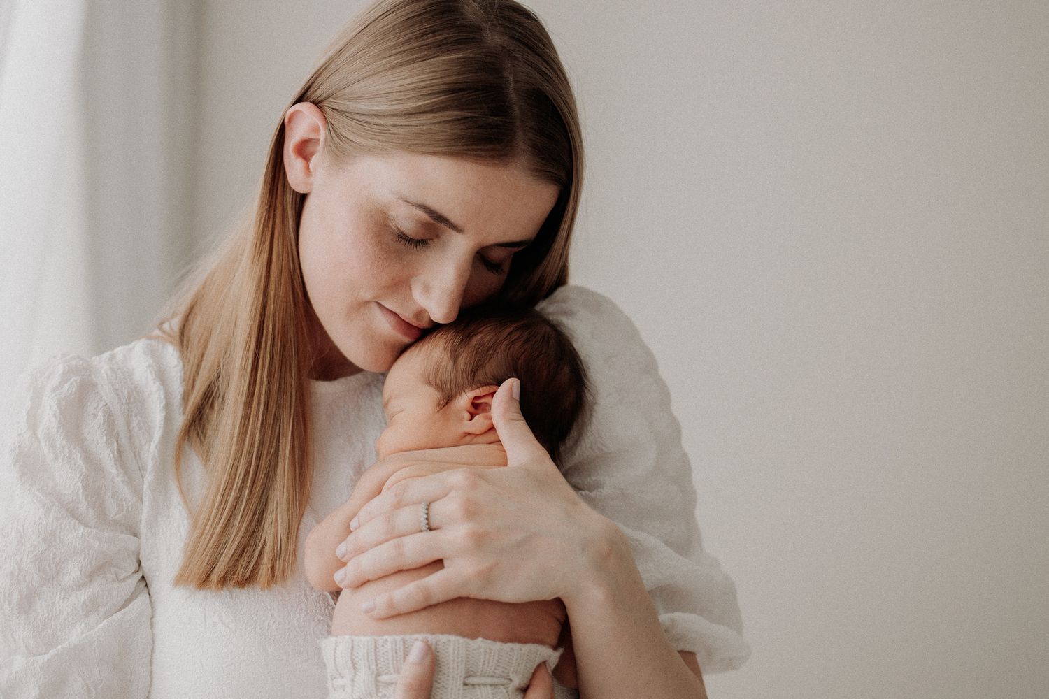 Äiti halaa vastasyntynyttä vauvaa sylissään studiossa Newborn kuvauksessa.