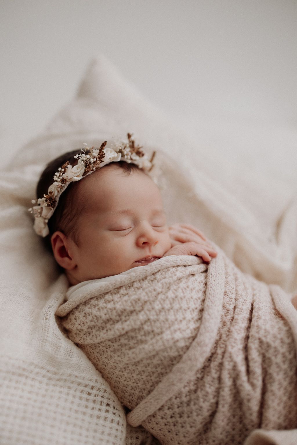 Vastasyntynyt vauva käärittynä vilttiin ja päässä kuivakukkapanta, vauva on newbornkuvauksessa Helsingin studiolla.