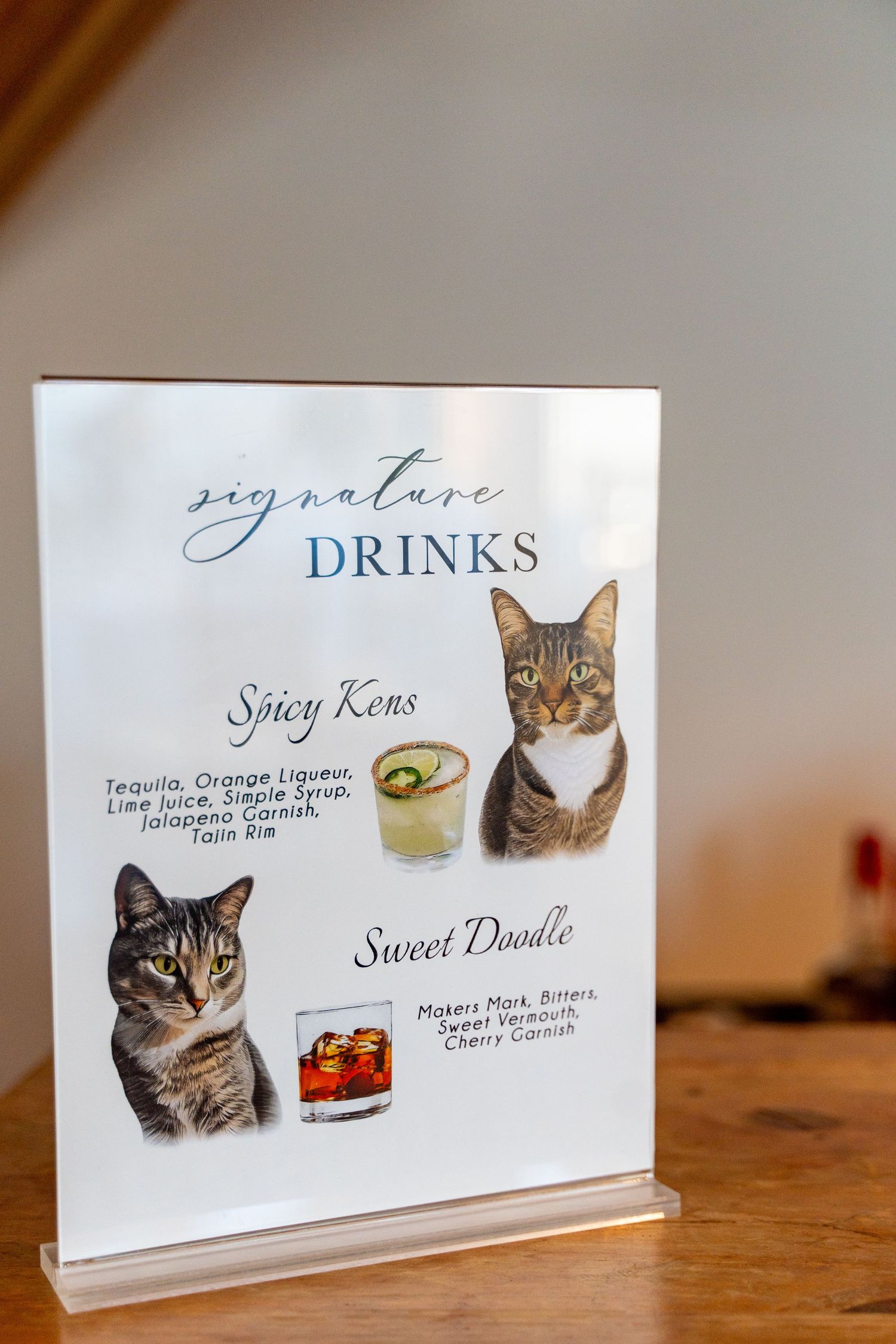 Signature drinks menu featuring illustrated cats with cocktail recipes on white display stand.