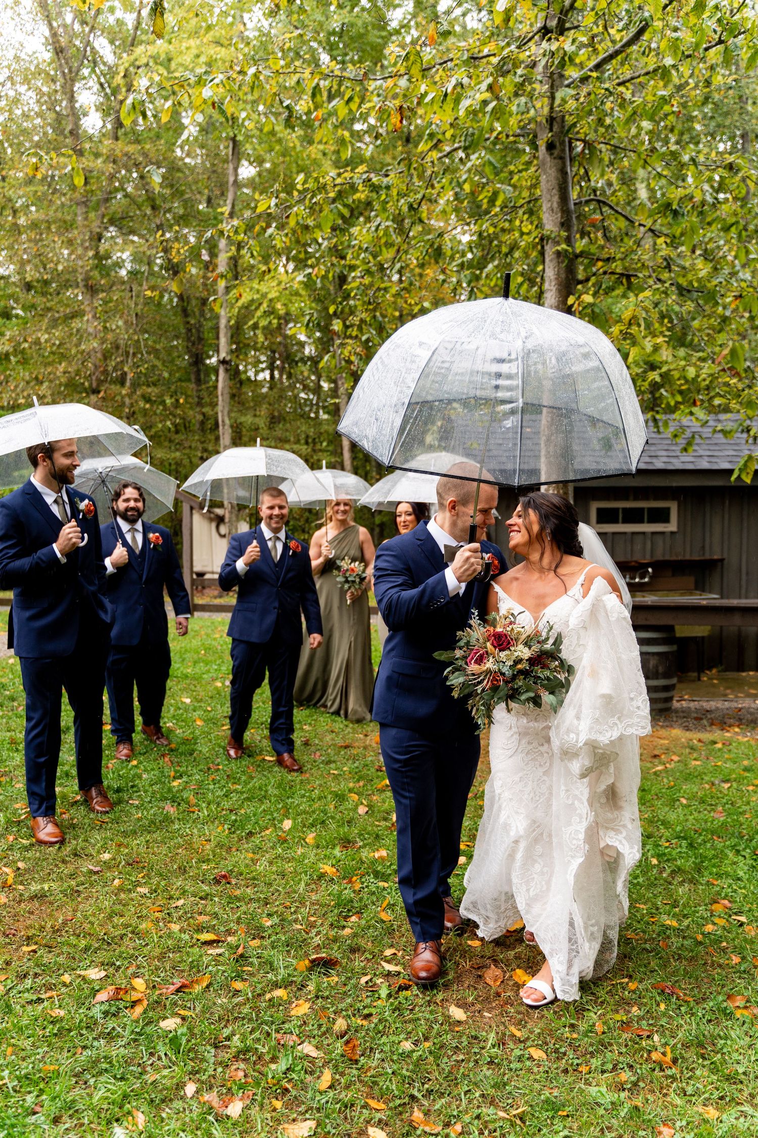 Wedding party celebrates with clear umbrellas on a rainy autumn day in an outdoor ceremony.
