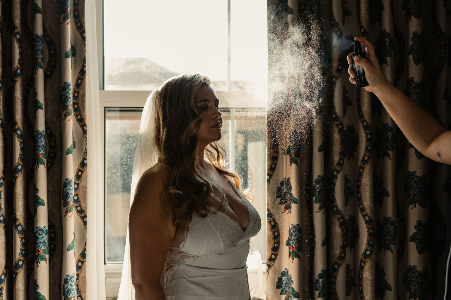 Wedding preparation with makeup artist spraying finishing touches.