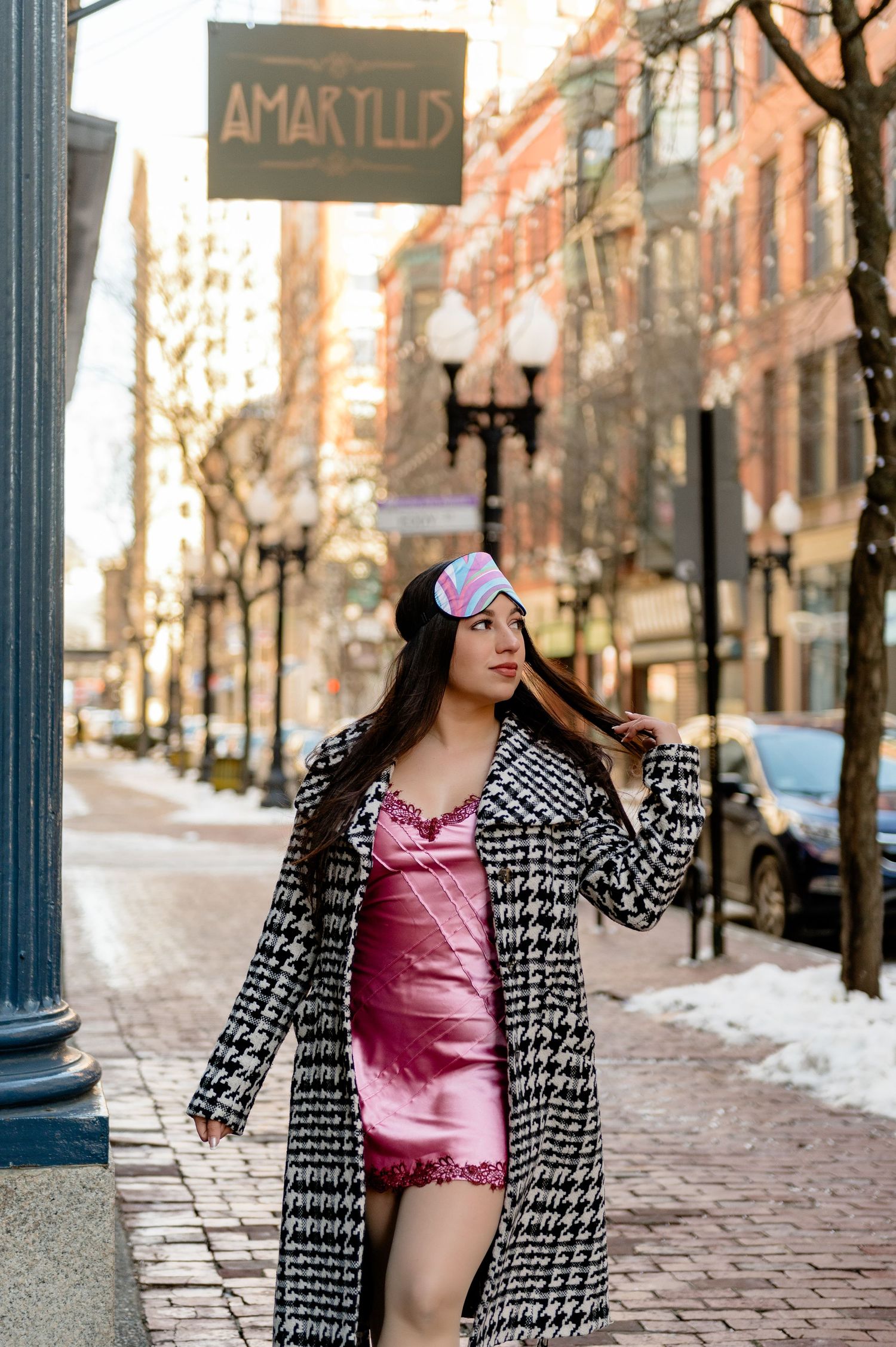 A winter fashion scene outside Amaryllis featuring a pink dress and houndstooth coat on a brick sidewalk.