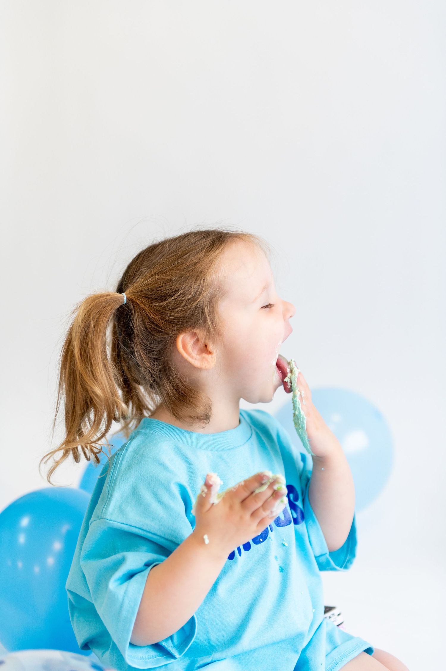 Child in light blue shirt laughing with joy surrounded by blue balloons.