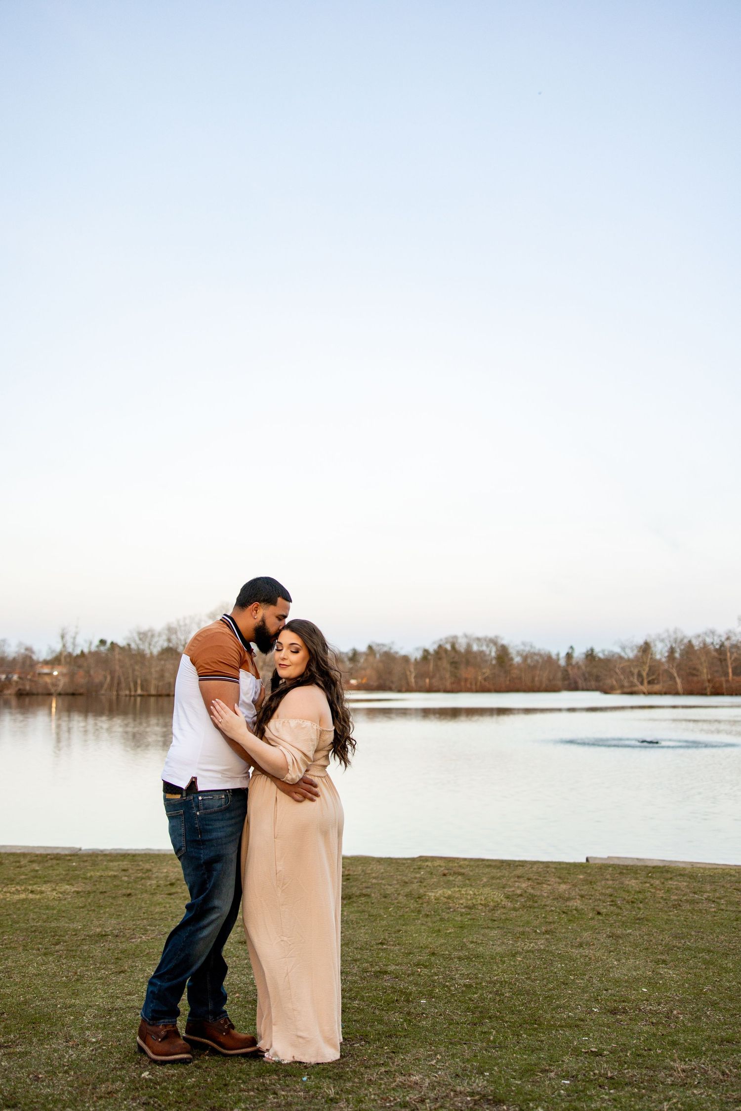 Couple embracing by a serene lake during golden hour.