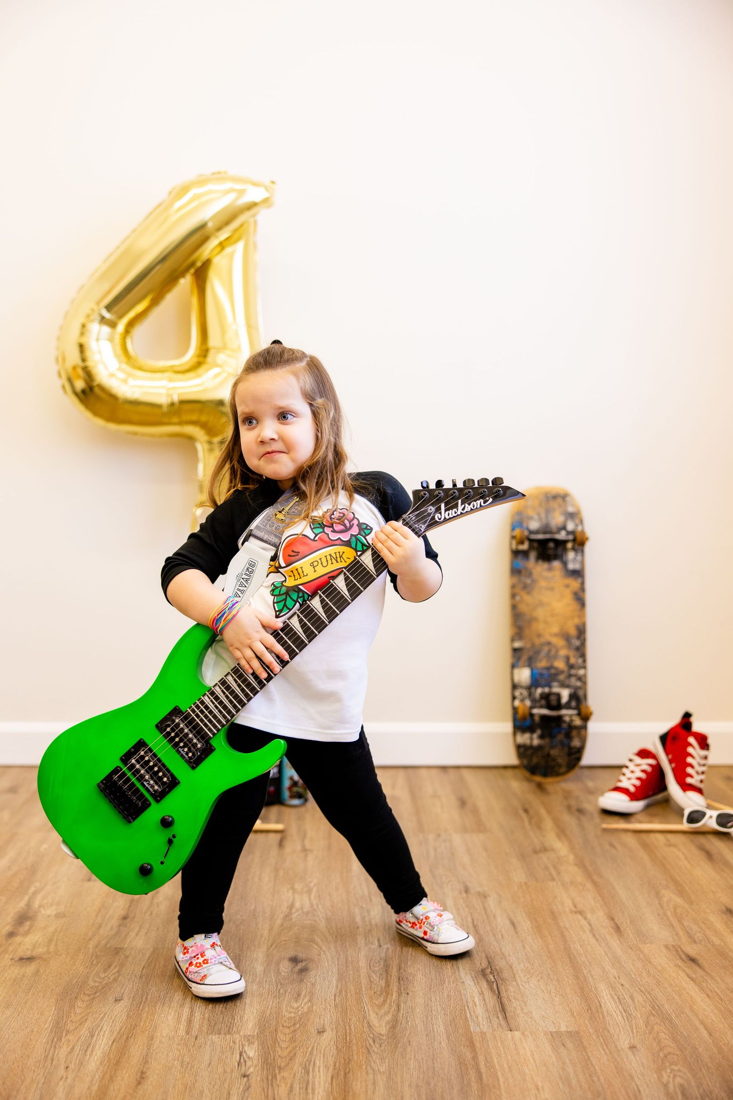 A child rocks out with a bright green electric guitar in front of a skateboard and gold number 4 balloon.