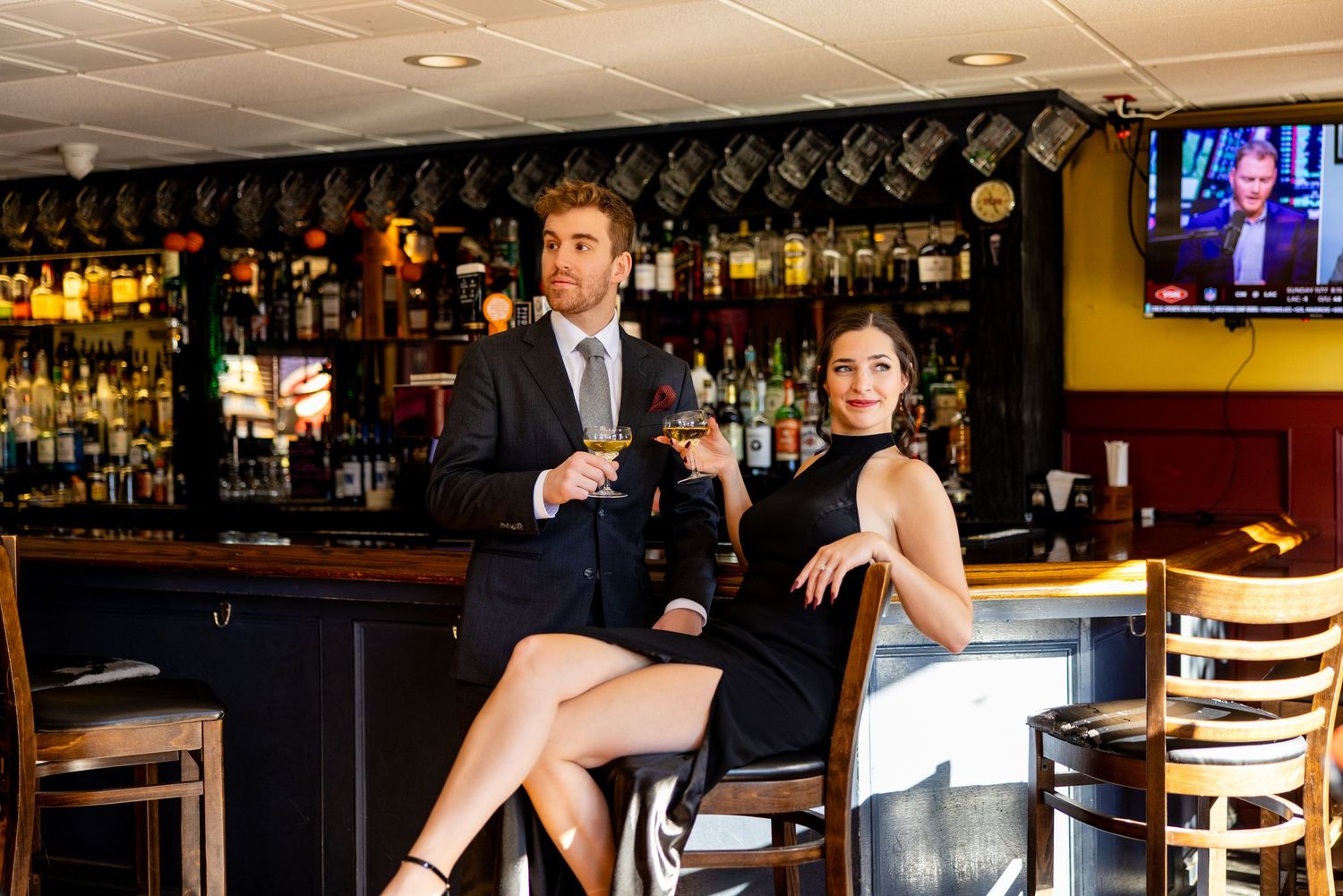 Stylish couple enjoys drinks at upscale bar with extensive liquor selection.