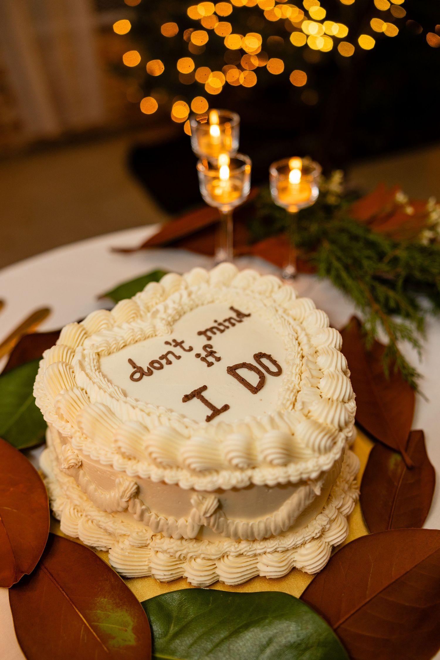 Heart-shaped wedding cake with 'I Do' written in frosting surrounded by candles and greenery.