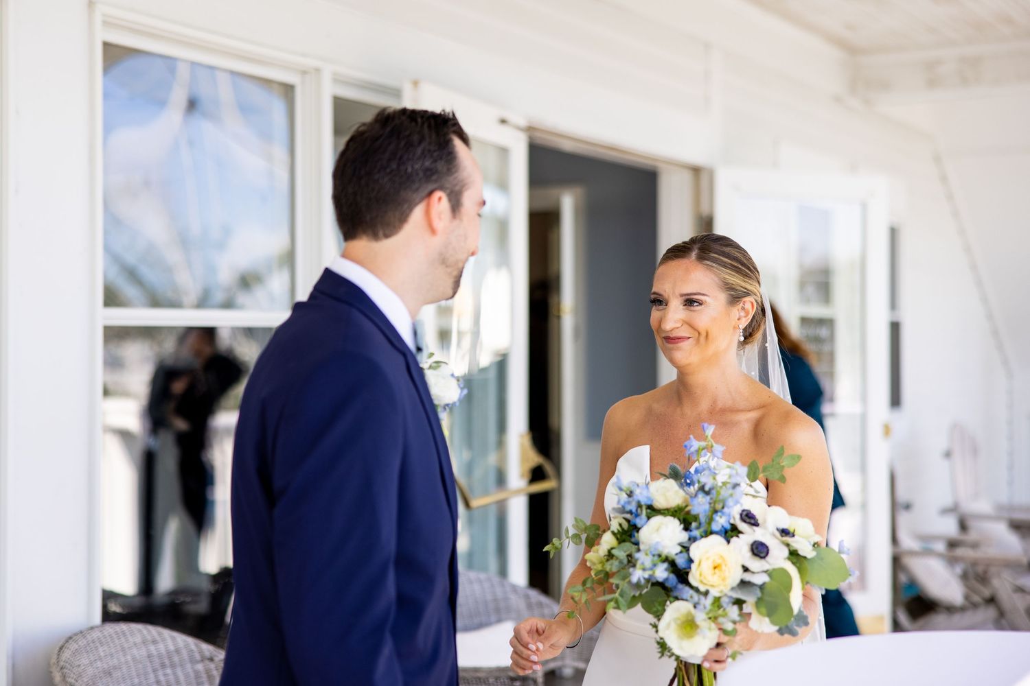Newlyweds share a special moment on a covered porch with white exterior and windows.
