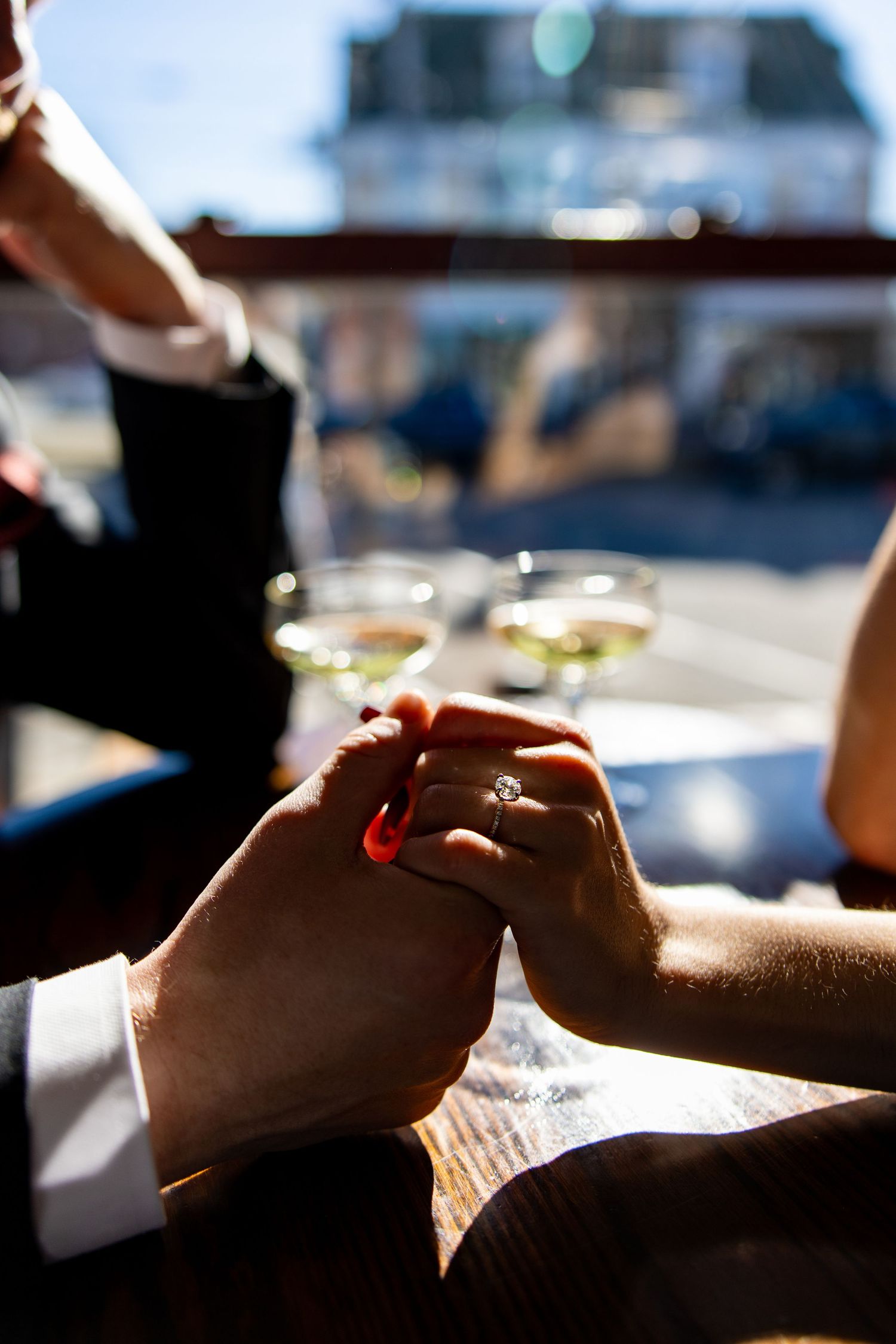Close-up of hands holding while cocktail glasses sit on a sunlit table.