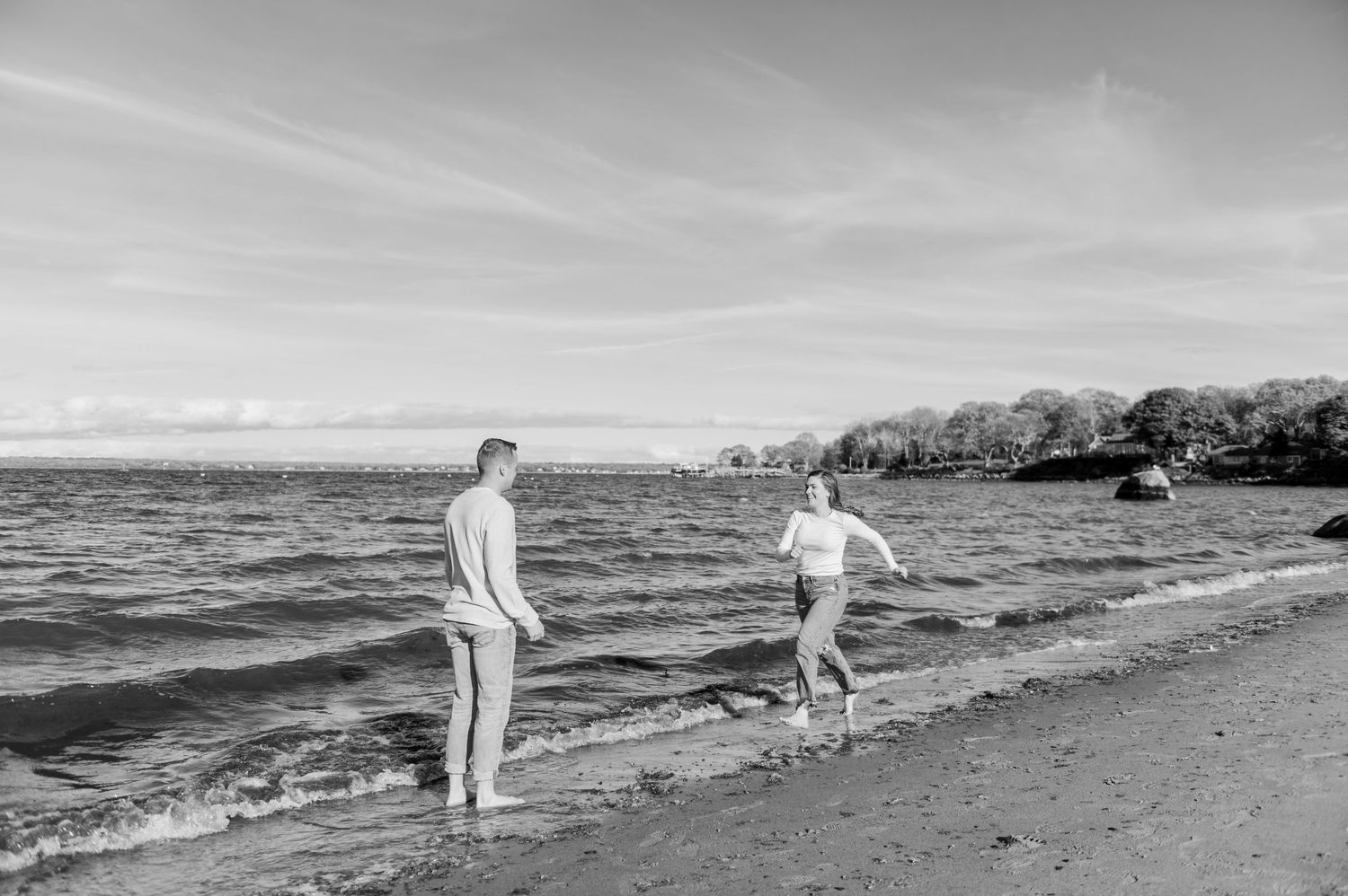 Two people walking along a peaceful beach shoreline in black and white.