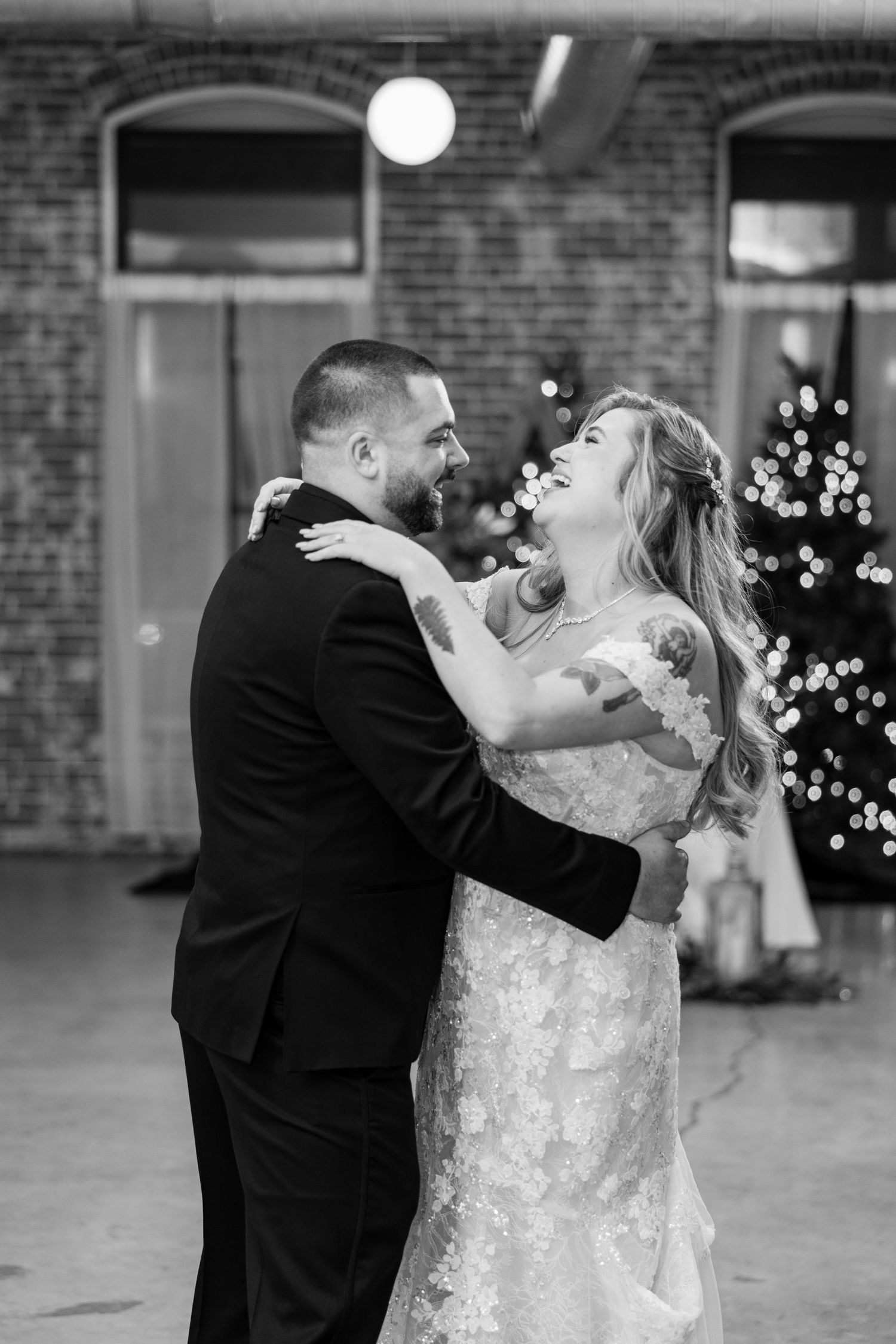 Wedding couple sharing a joyful moment during their first dance in front of a brick wall.