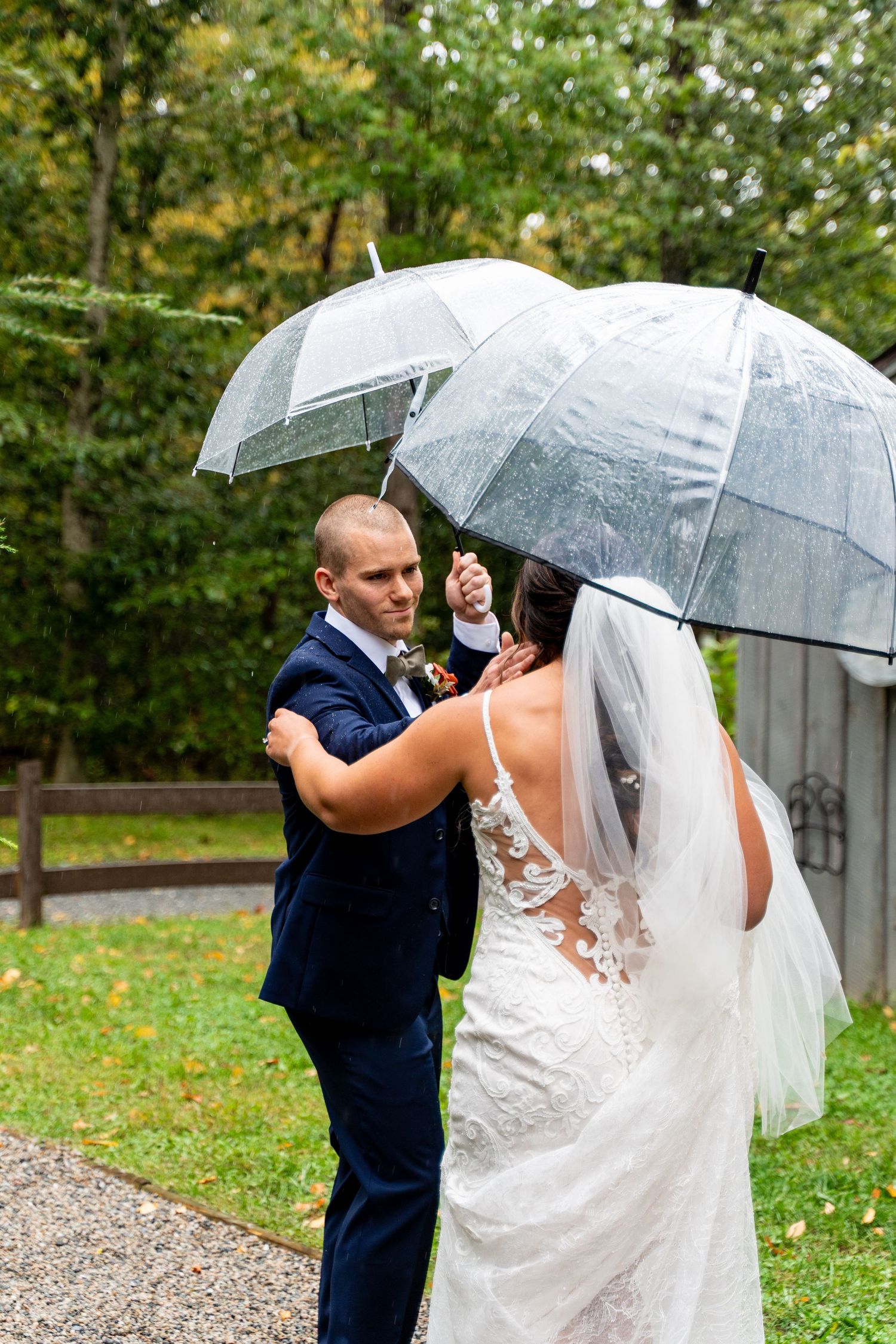 Wedding couple sharing intimate moment under clear umbrellas in garden setting.