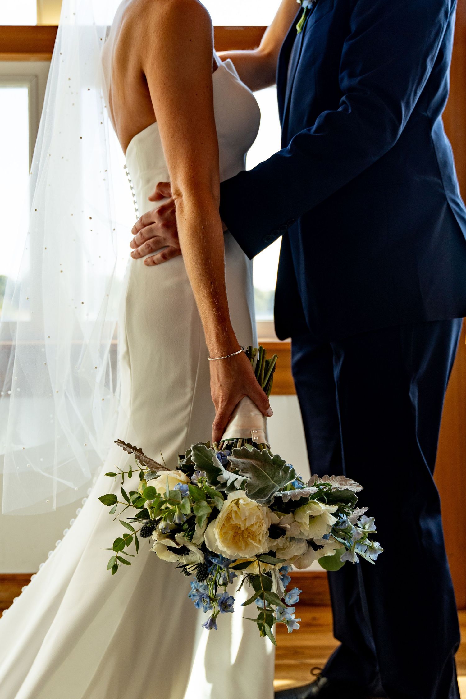 Close-up of elegant wedding attire with white gown, navy suit and floral bouquet.