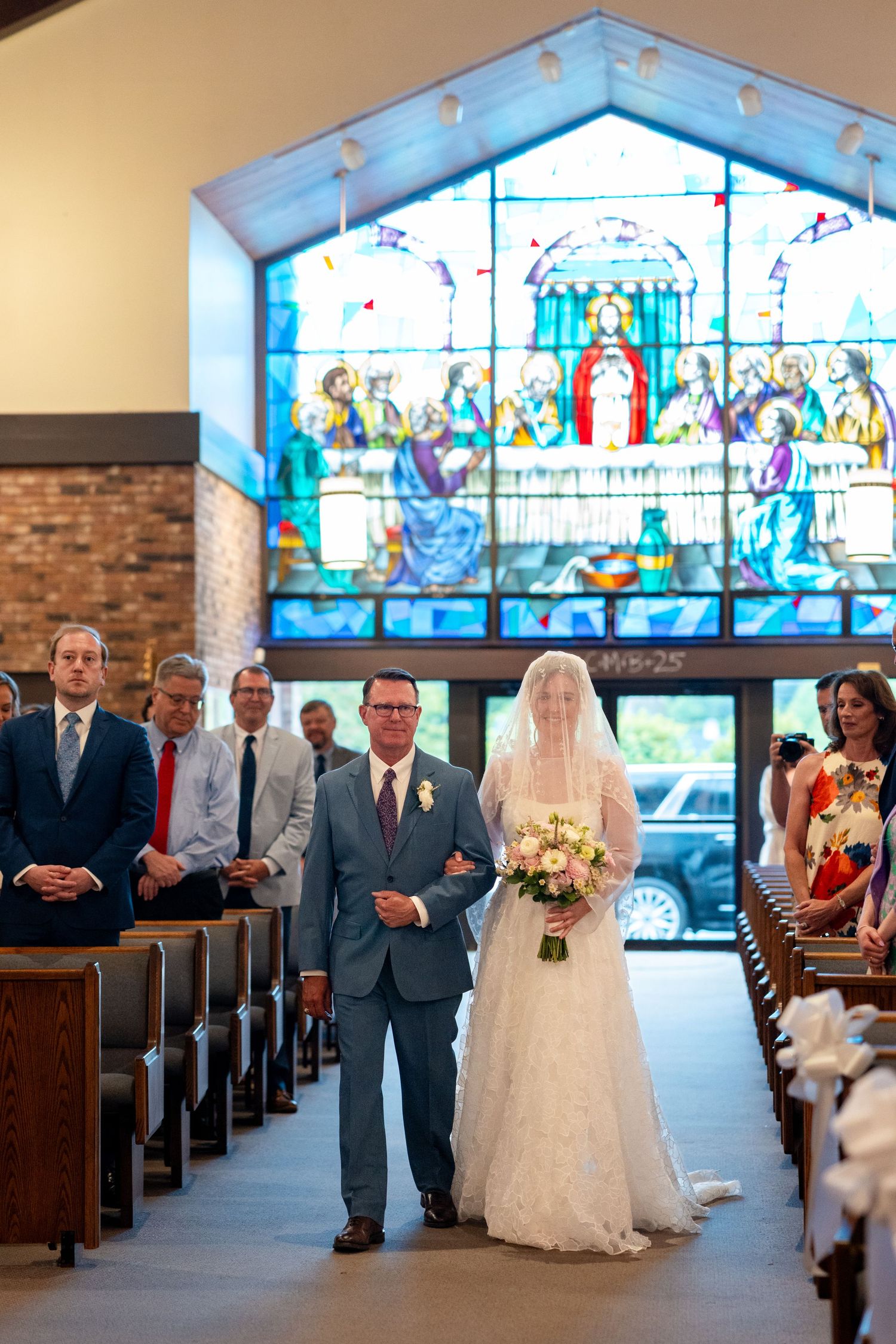 Church wedding ceremony with a beautiful stained glass window backdrop featuring a religious scene in blue and white tones.